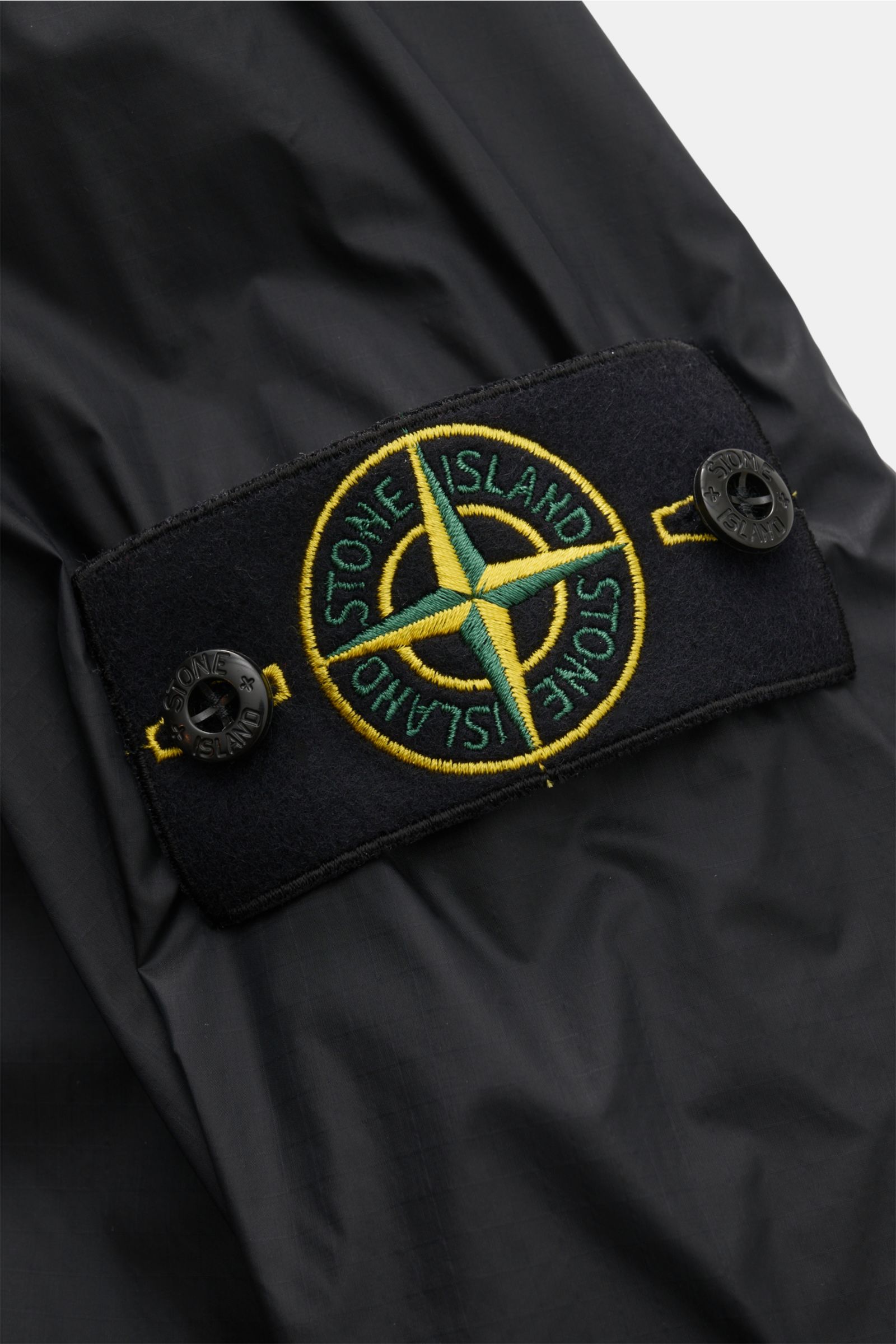 Close-up view of the Stone Island Blouson 'Light Ripstop Cordura' black showing the embroidered logo patch on high-strength ripstop fabric, robust yet lightweight with a smooth feel, slim fit, two-way zip, drawstring hood, three front pockets, elastic hem