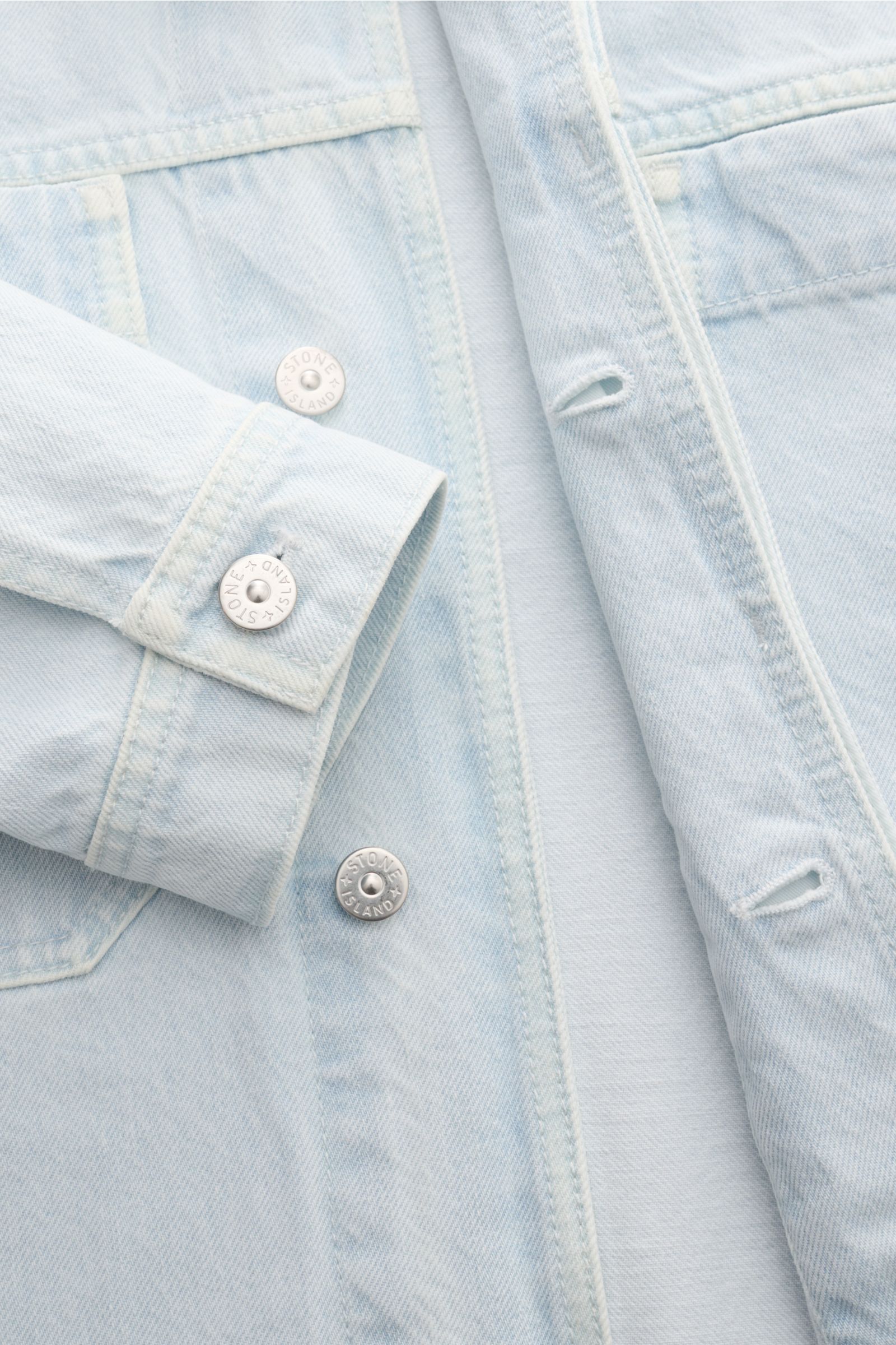 Stone Island Denim jacket pastel blue shown from a close-up front perspective, highlighting buttons, cuffs, and denim fabric texture.