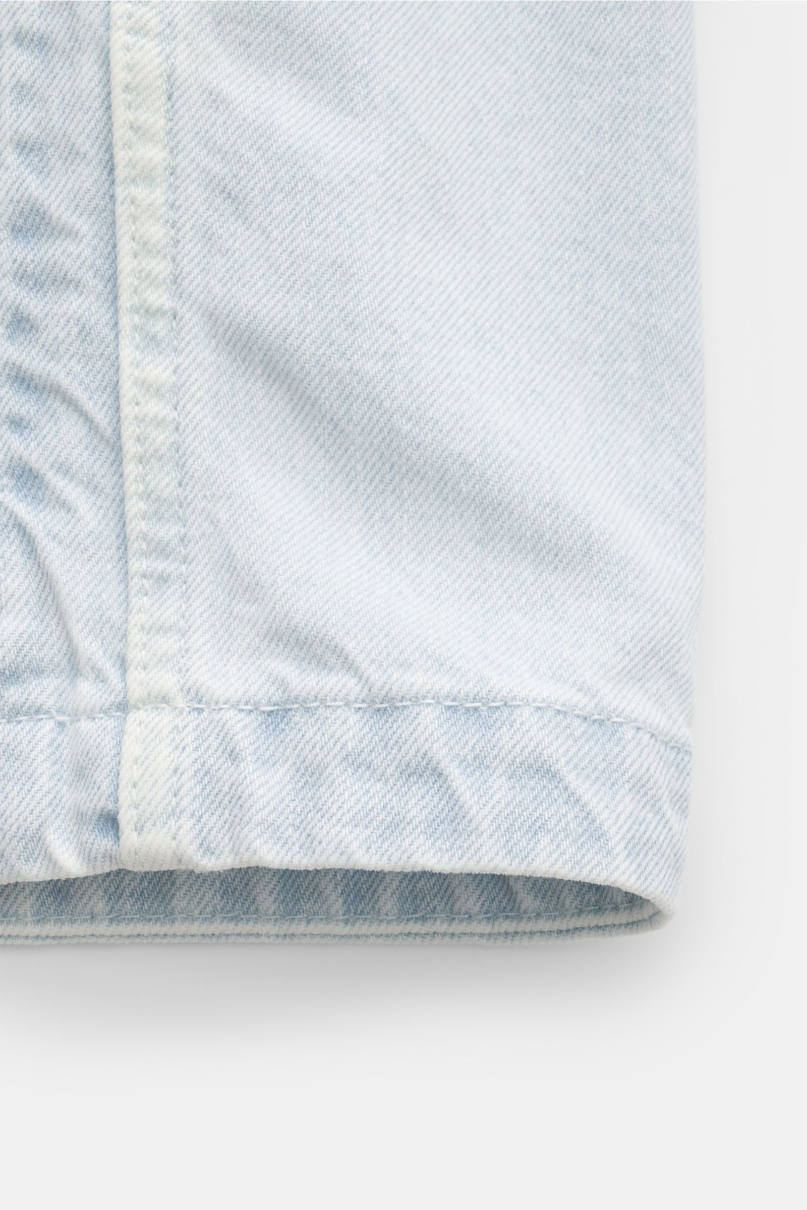 Stone Island Denim jacket pastel blue close-up of the hem and seam, showing pure cotton denim texture from a side perspective; a timeless companion for urban spring outfits with a straight cut, patch front pockets, slim fit, concealed button placket, turn