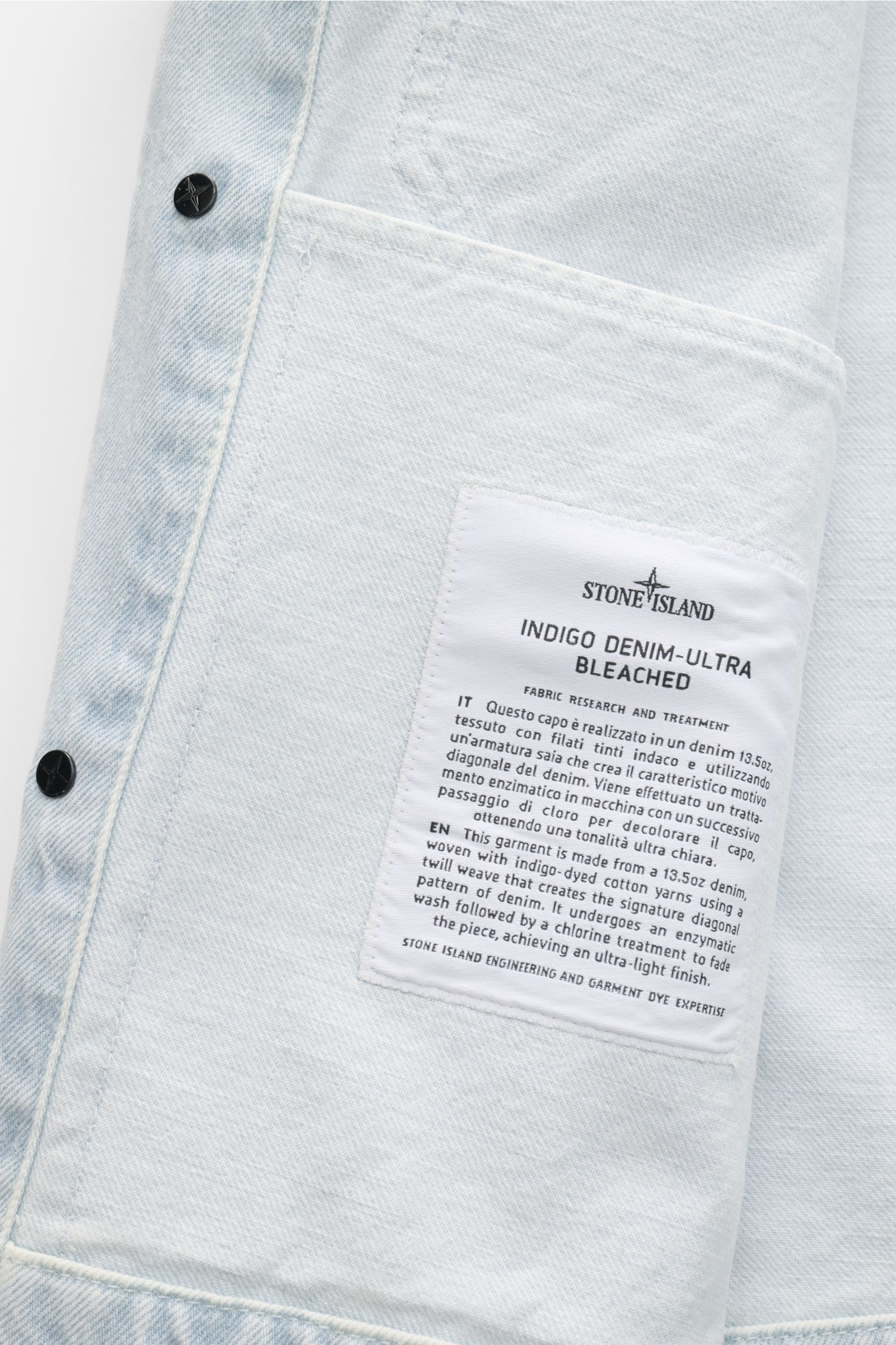 Stone Island Denim jacket pastel blue shown close-up from the inside, featuring a white label with fabric and treatment details in black text. A timeless companion for urban spring outfits: This denim jacket from the STONE ISLAND 'Denim' capsule collectio