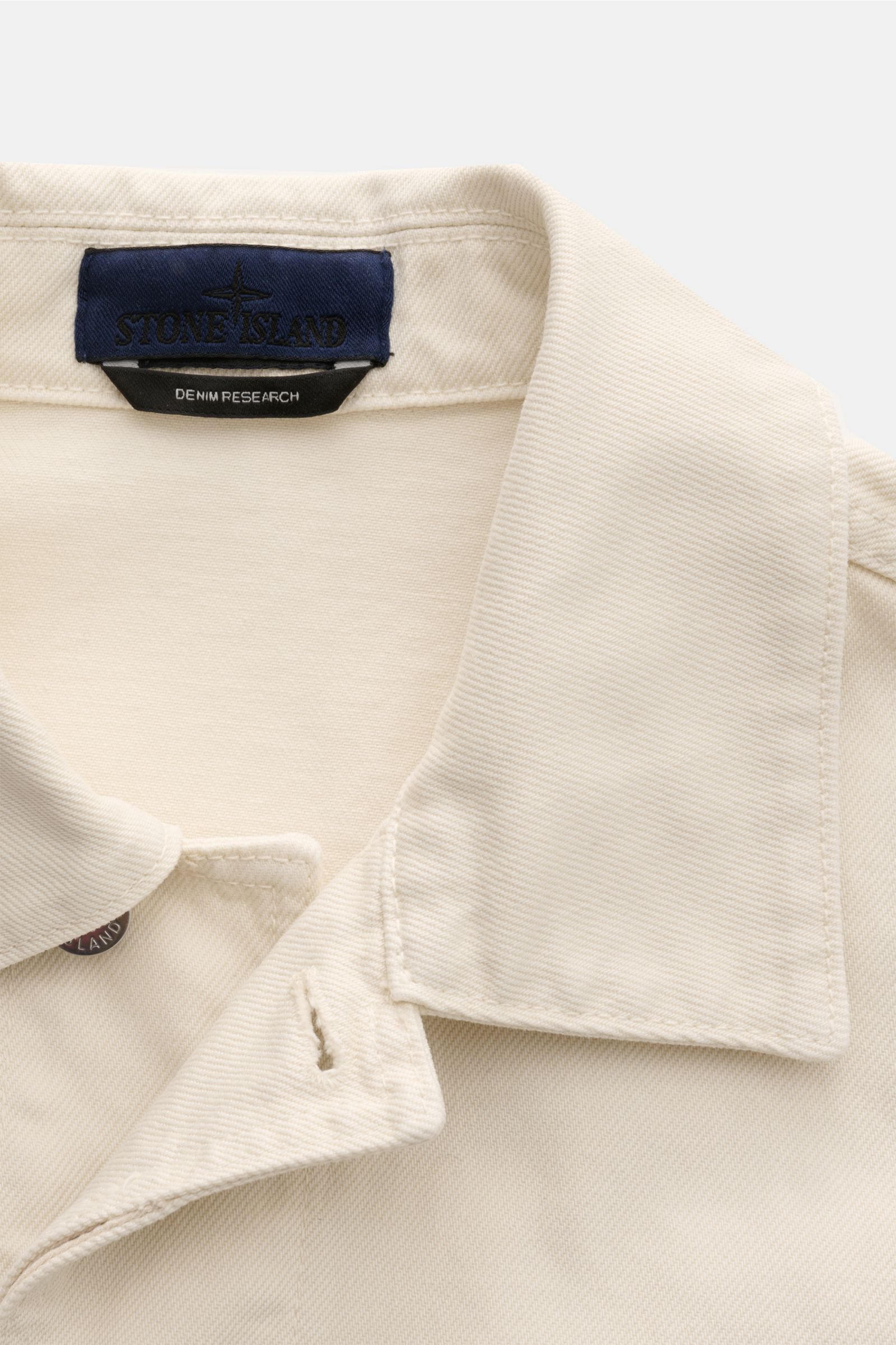 Stone Island Jeansjacke 'Light Bull Denim-TC' creme, Detailansicht des Umlegekragens aus leichtem, wasserabweisendem Denim mit Kompass-Badge.