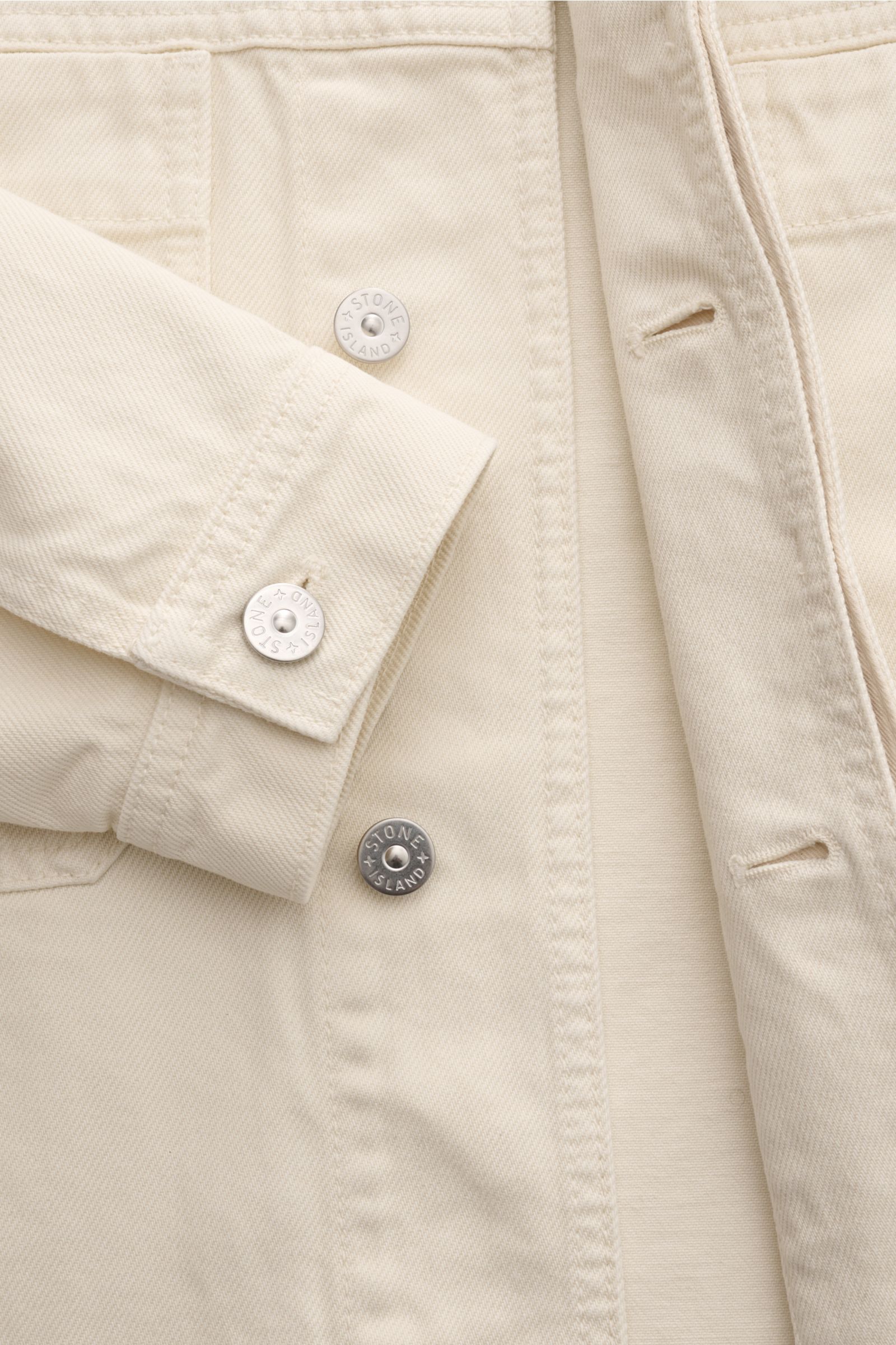 Stone Island Jeansjacke 'Light Bull Denim-TC' creme, Nahaufnahme von Ärmel, verdeckter Knopfleiste, weichem Baumwoll-Denim und Kompass-Badge.