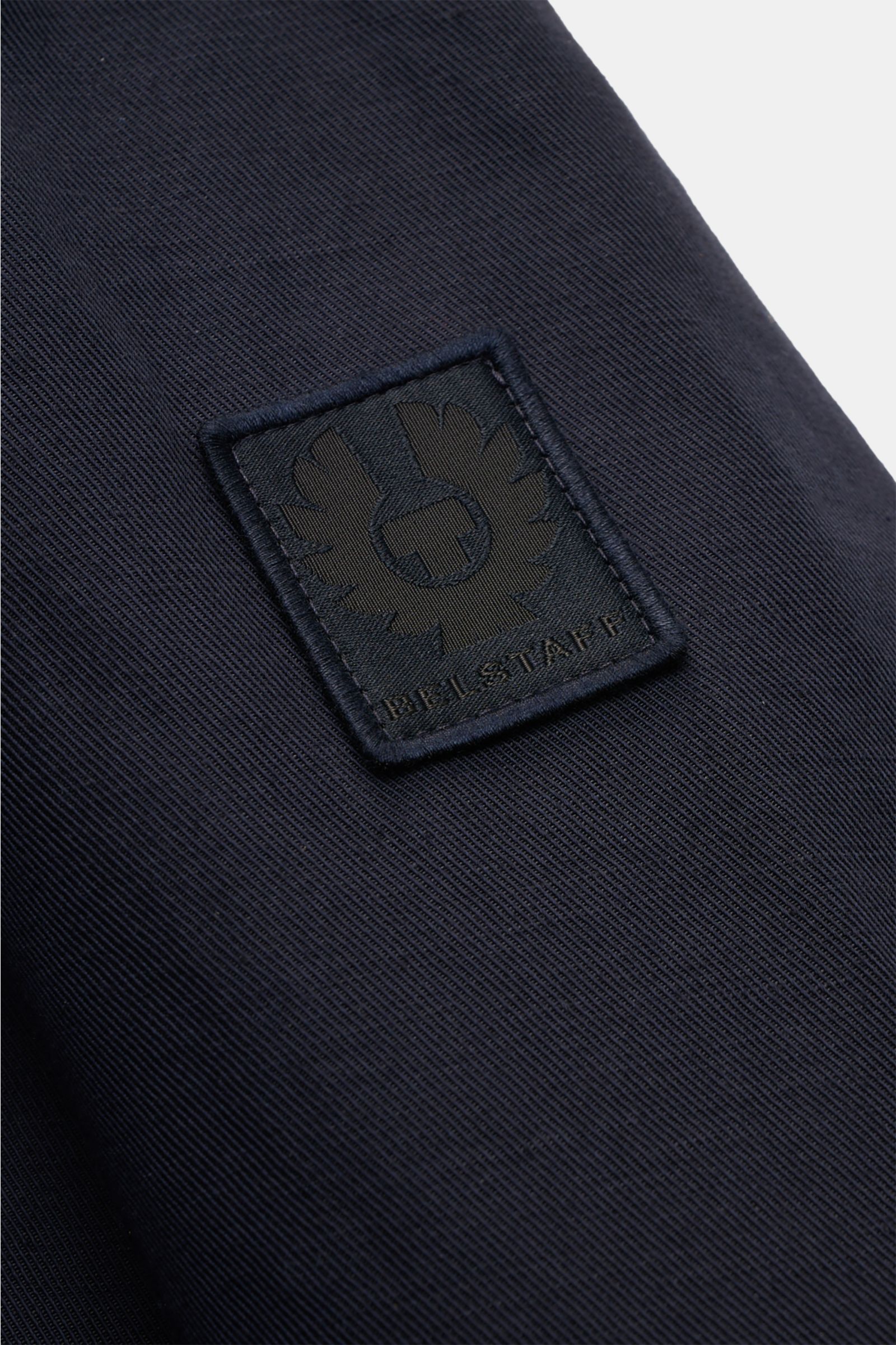 Nahaufnahme des tonalen BELSTAFF-Weblabels auf dem Ärmel des Belstaff Blouson 'Helston' navy aus Leinen-Baumwoll-Twill.