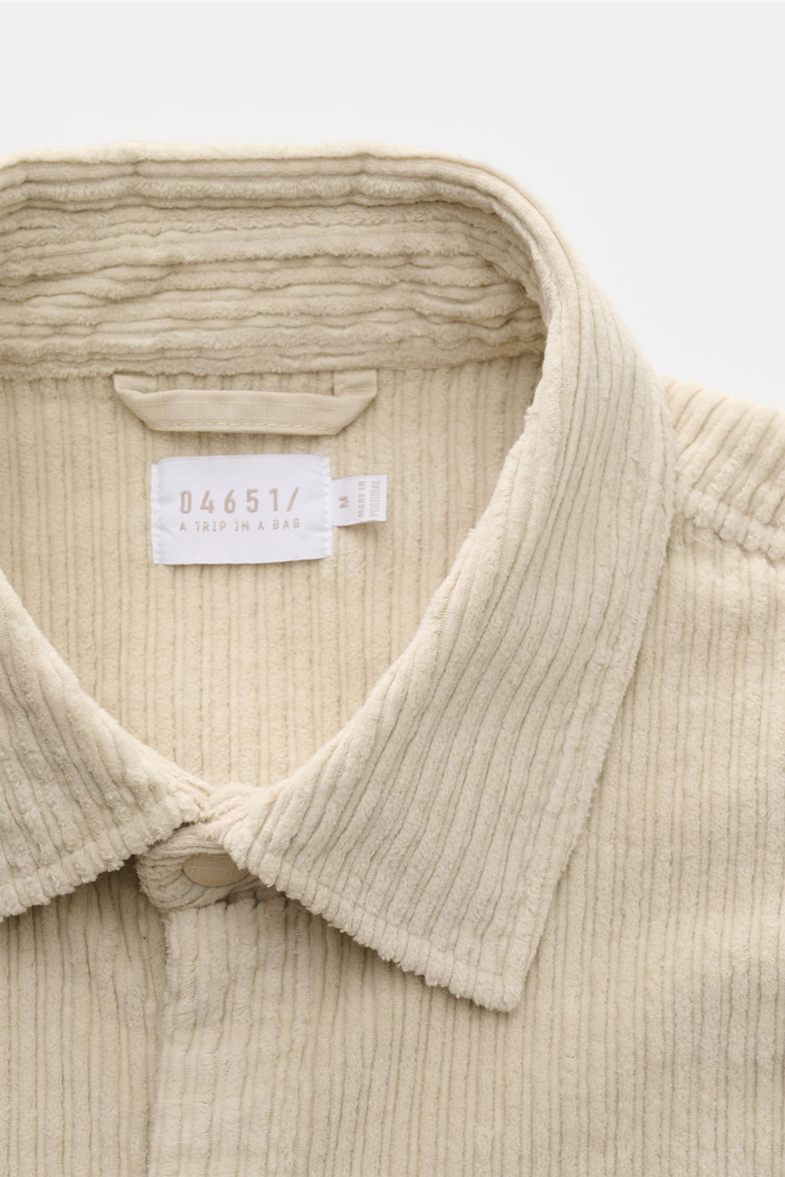 Nahaufnahme des Kragens und der Knopfleiste vom 04651/ A trip in a bag Cord-Overshirt sand aus sandfarbenem Baumwoll-Cord, von oben fotografiert.