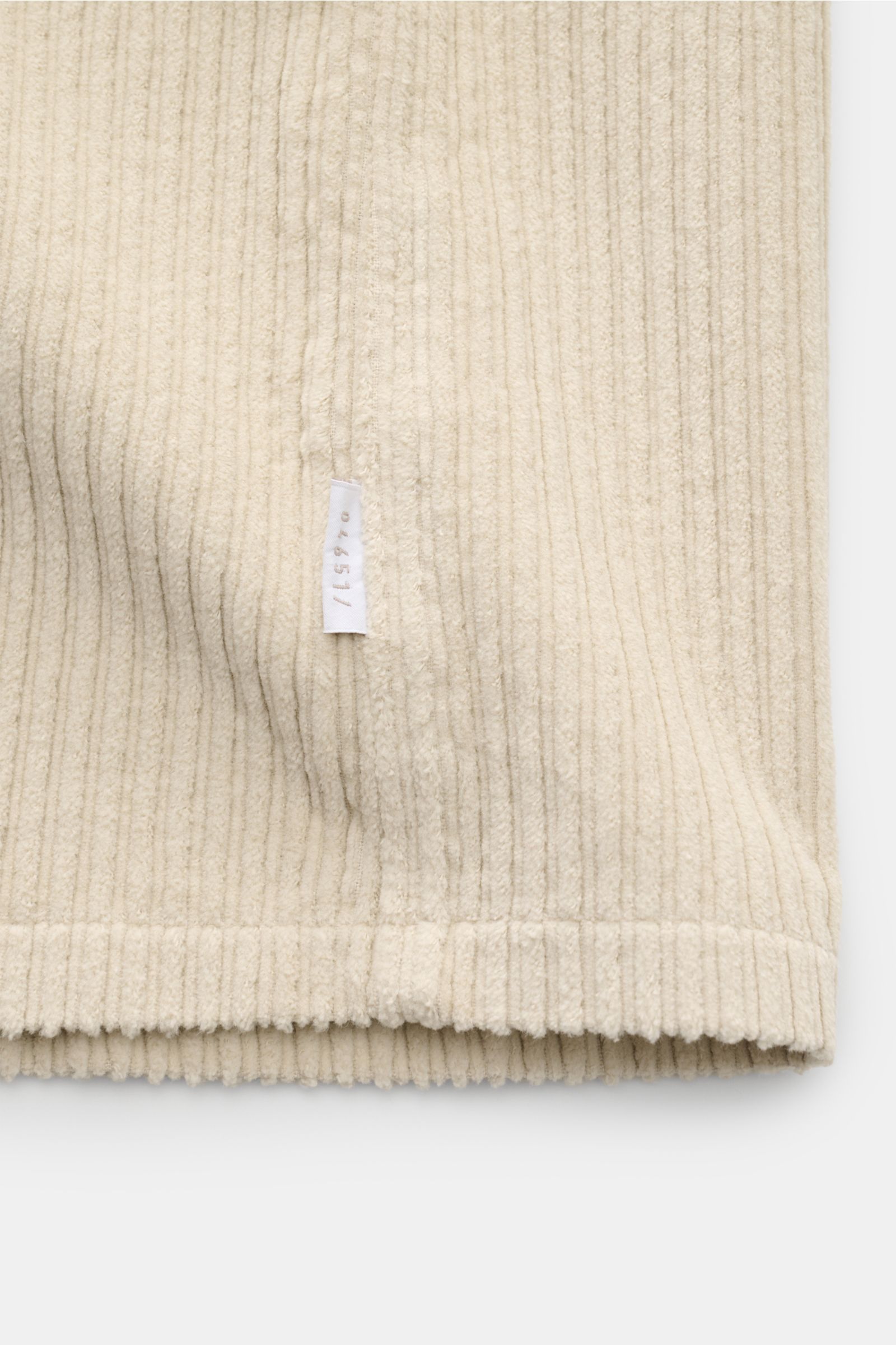 Nahaufnahme des sandfarbenen 04651/ A trip in a bag Cord-Overshirts, Detailansicht der Baumwoll-Cordstruktur und kleinem Weblabel an der Seitennaht.