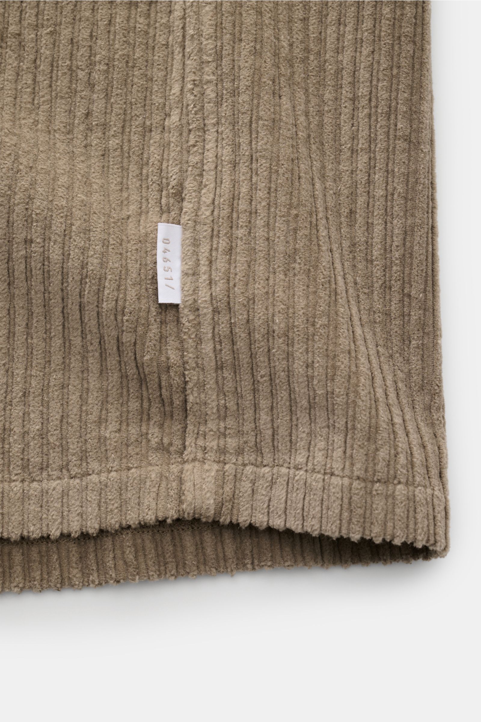 04651/ A trip in a bag Cord-Overshirt taupe, Detailaufnahme der unteren Kante und Seitennaht mit kleinem Weblabel aus Baumwoll-Cord.