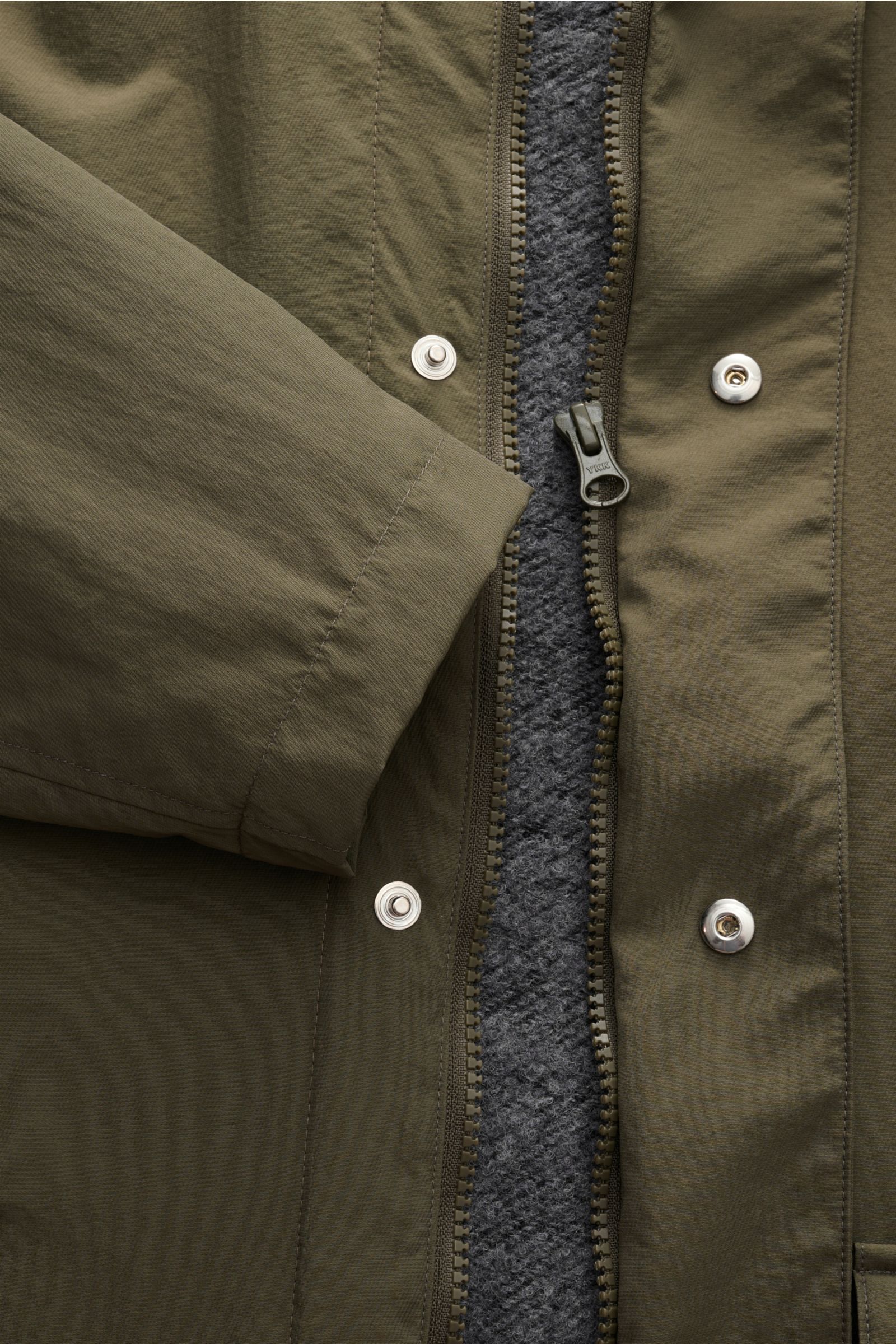 Nahaufnahme des olivfarbenen 04651/ A trip in a bag Parka 'The Coat' mit offenem Reißverschluss, Knöpfen, Kapuze und grauem Futter.