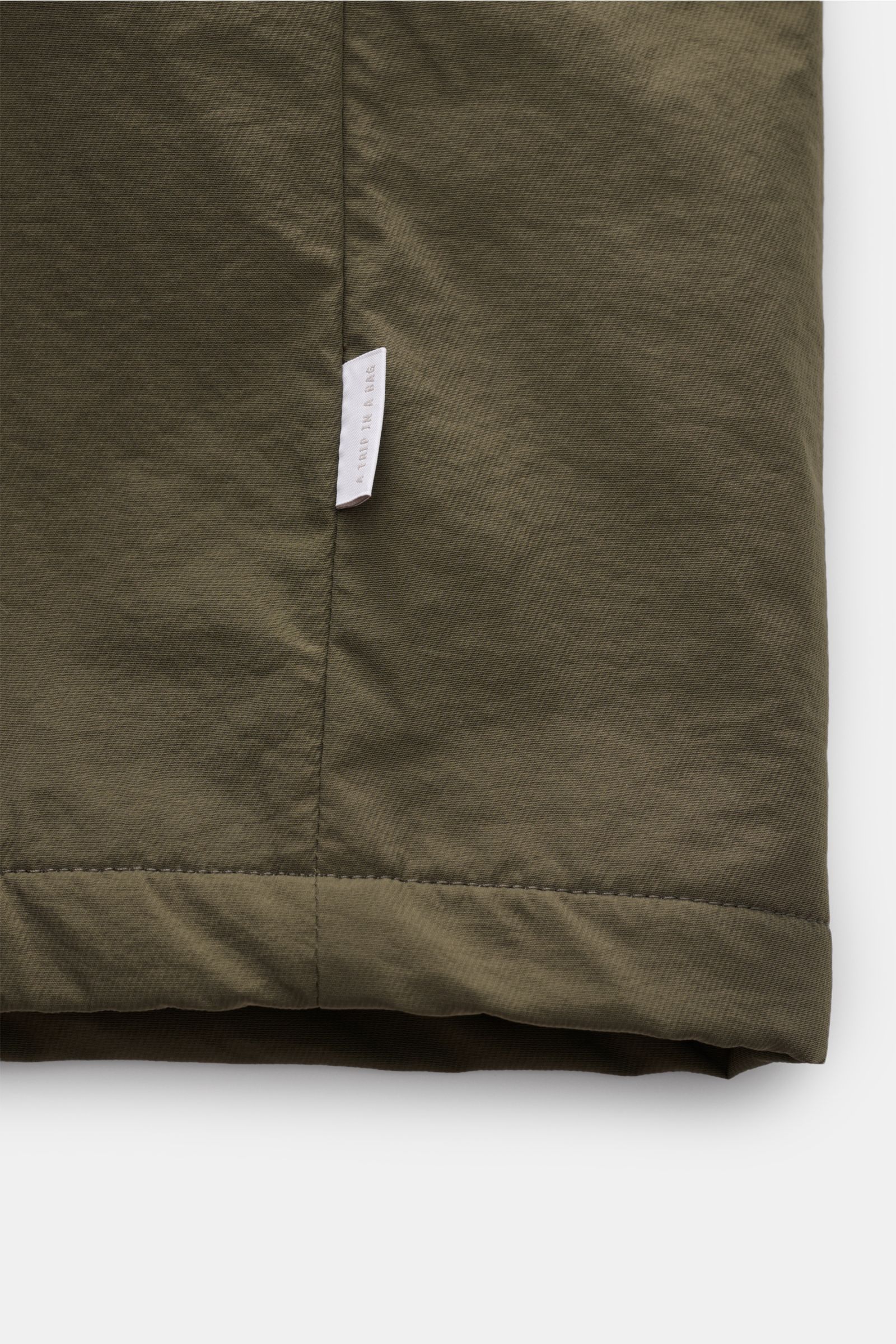 Nahaufnahme des Saums mit Logo-Weblabel des 04651/ A trip in a bag Parka 'The Coat' oliv aus hochwertiger Microfaser.
