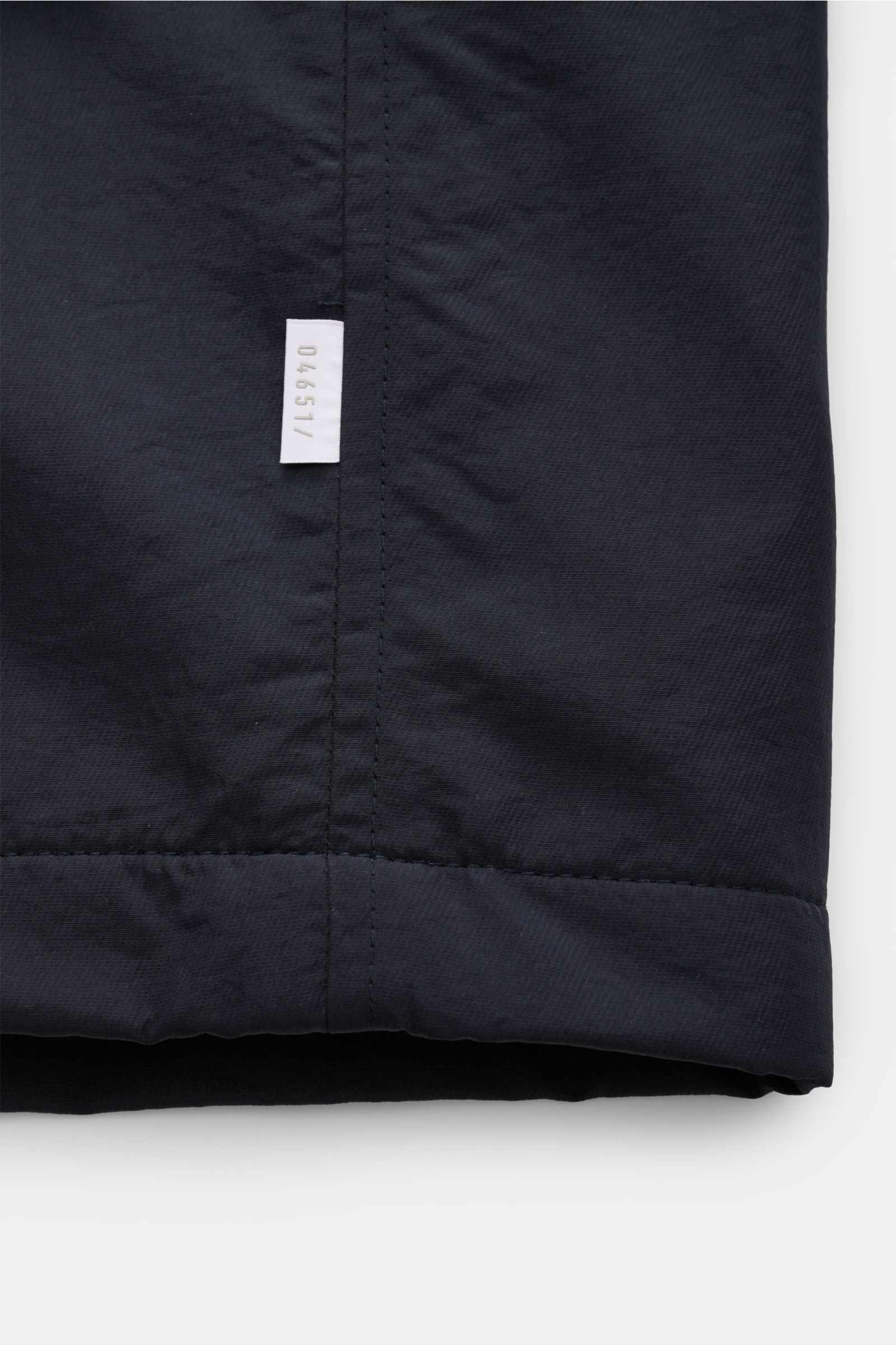 Close-up front view of the hem of the 04651/ A trip in a bag Jacket dark navy showing high-quality microfibre fabric, smooth feel, lightweight padding, wind and water repellent, regular fit, zip, concealed hood in collar, raglan sleeves, hip pockets with 