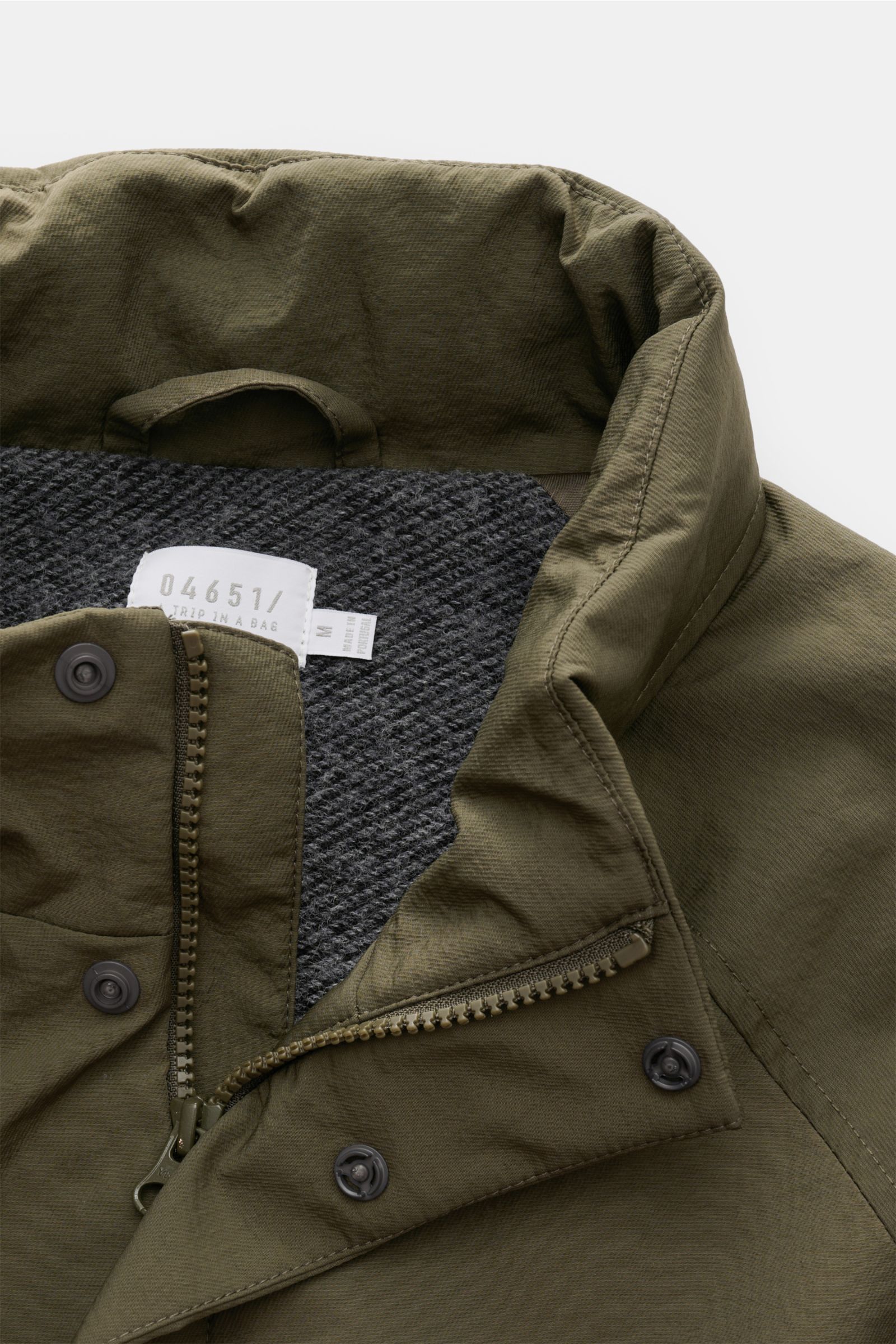 Close-up front view of the 04651/ A trip in a bag Jacket olive showing high-quality microfibre, smooth feel, lightweight padding, wind and water repellent, regular fit, zip, concealed hood in collar, raglan sleeves, hip pockets with flap, small woven labe