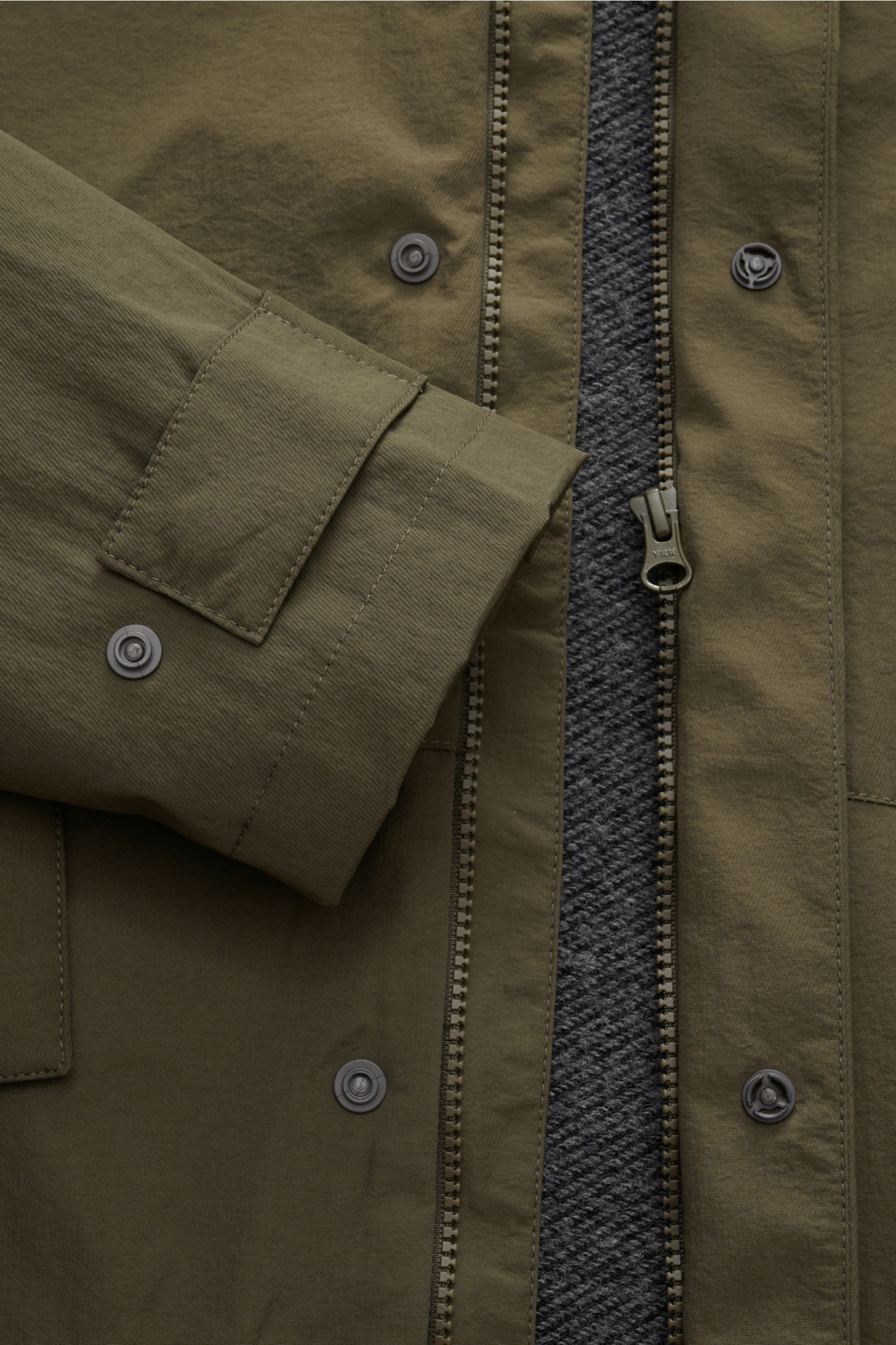 Close-up front view of the 04651/ A trip in a bag Jacket olive showing high-quality microfibre, smooth feel, lightweight padding, wind and water repellent fabric, regular fit, zip, concealed hood in collar, raglan sleeves, hip pockets with flap, small wov
