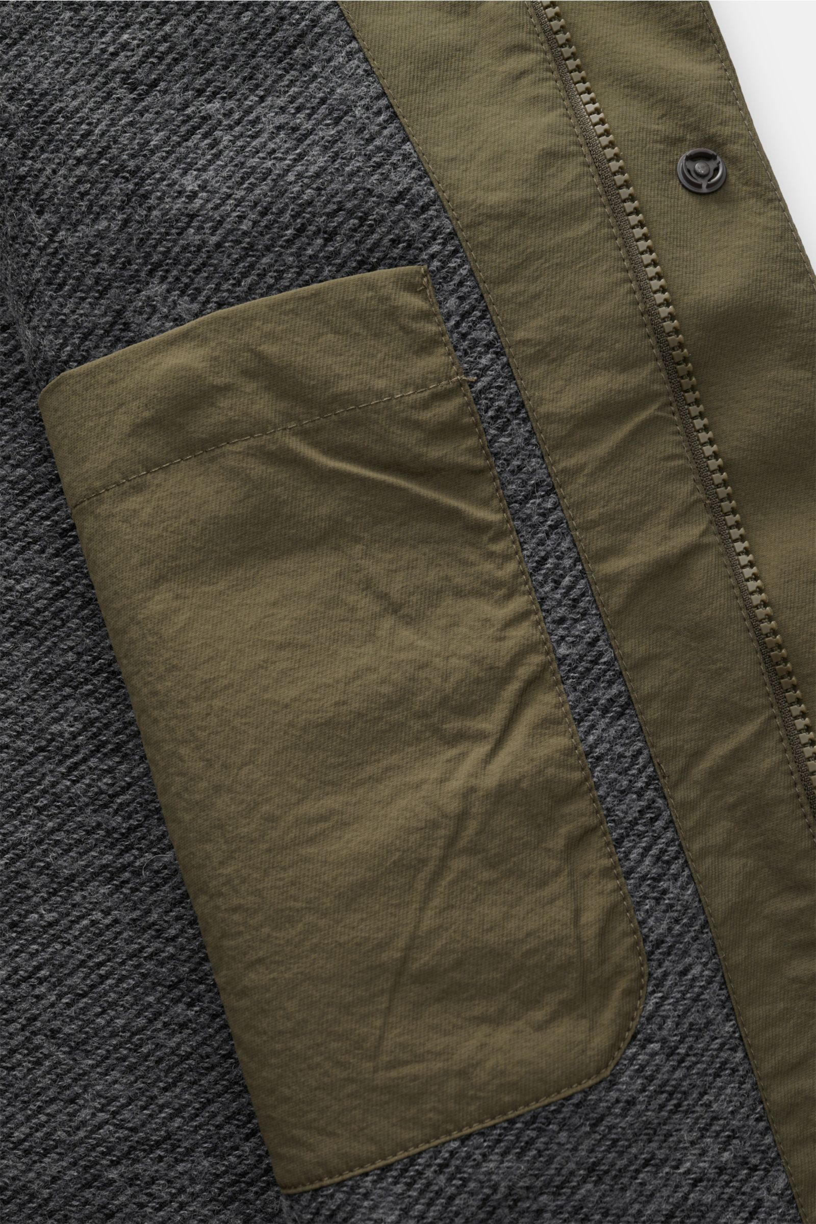 Close-up image of the inside of the 04651/ A trip in a bag Jacket olive, showing the lining made of a wool blend and an inside pocket, photographed from above. Features include high-quality microfibre, smooth feel, lightweight padding, wind and water repe