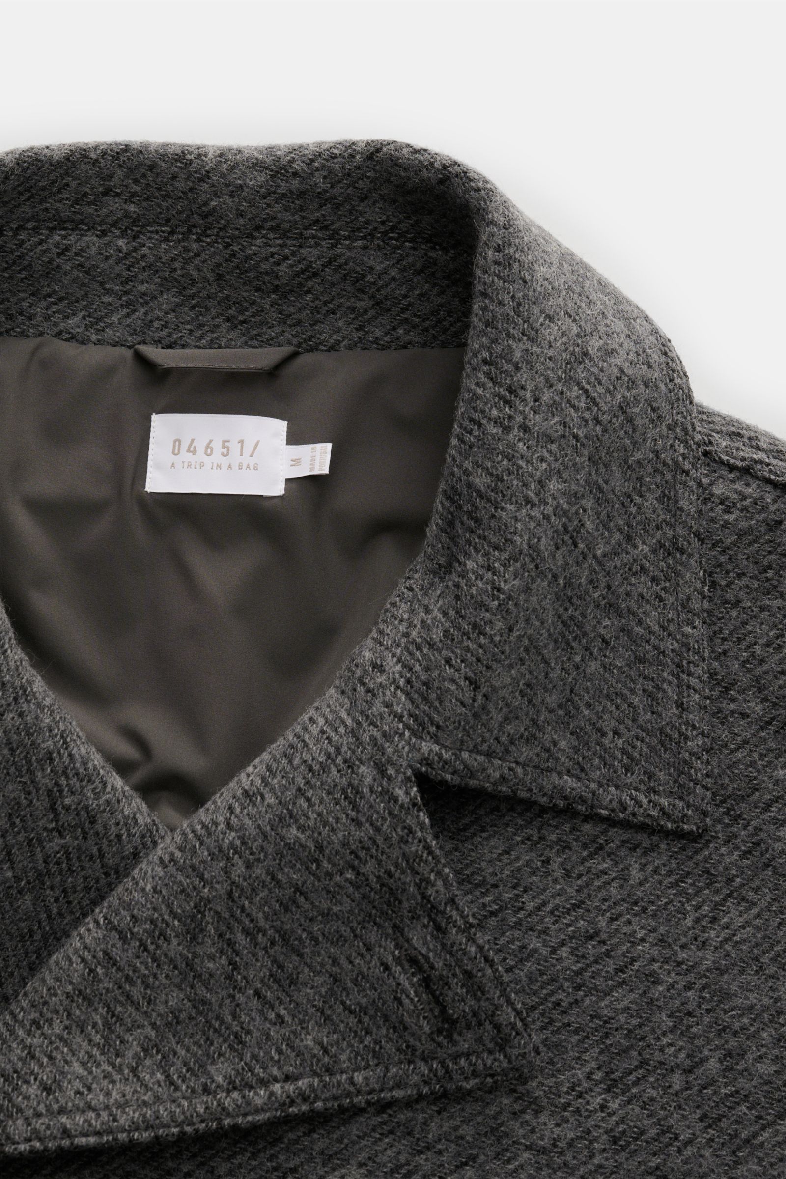Nahaufnahme der dunkelgrau melierten 04651/ A trip in a bag Cabanjacke aus Woll-Microfaser-Mix mit Slim Fit, zweireihiger Drei-Knopf-Leiste, variablem Reverskragen, schrägen Leistentaschen, glattem Futterstoff und einer Innentasche, fotografiert von oben.