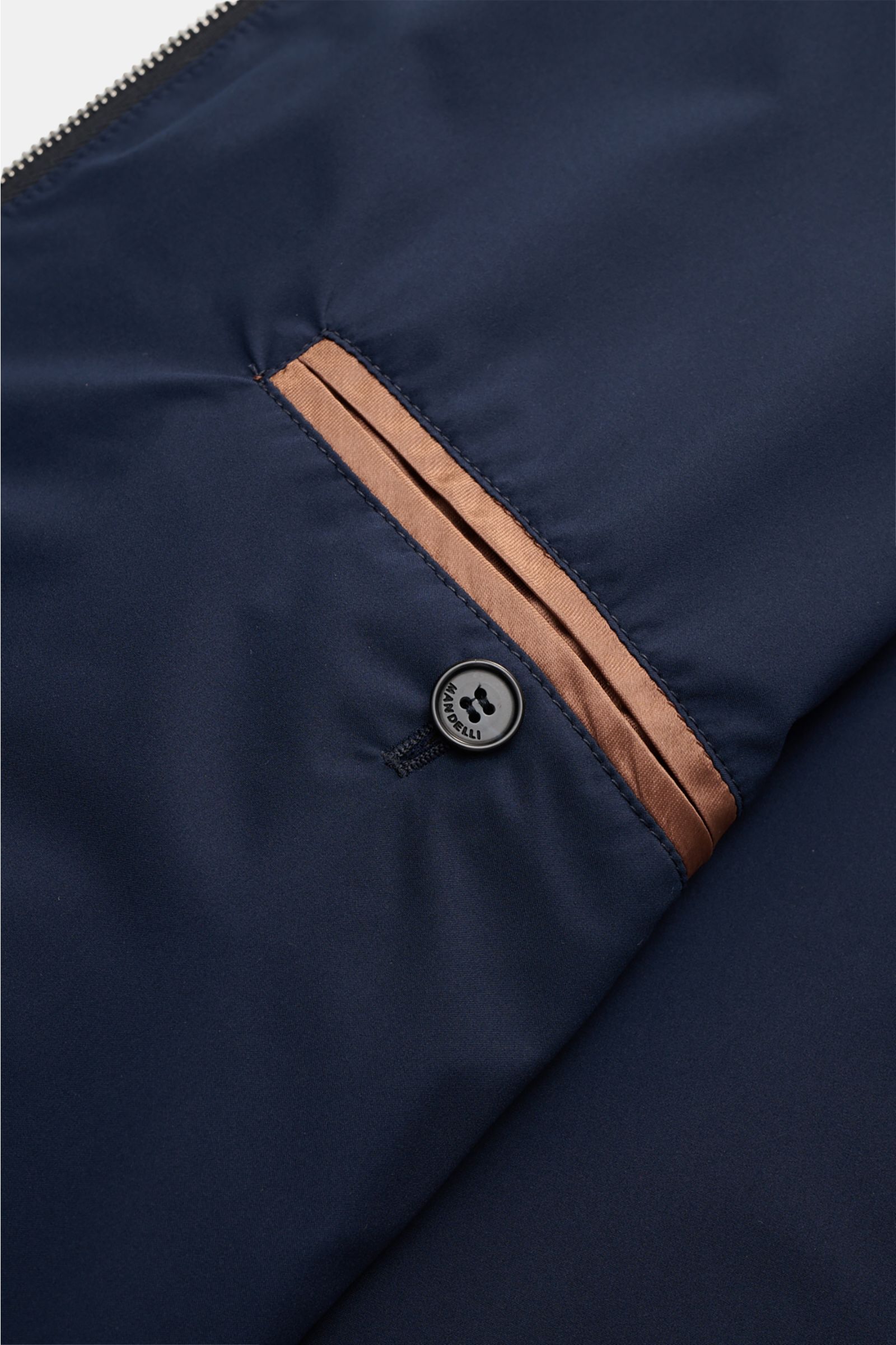Close-up front detail of the Mandelli Blouson navy showing a button and brown-trimmed pocket, photographed from above; elegant ease for transitional period, pure wool, smooth feel, slim fit, two-way zip, standing collar, elastic hem and sleeve cuffs, smoo