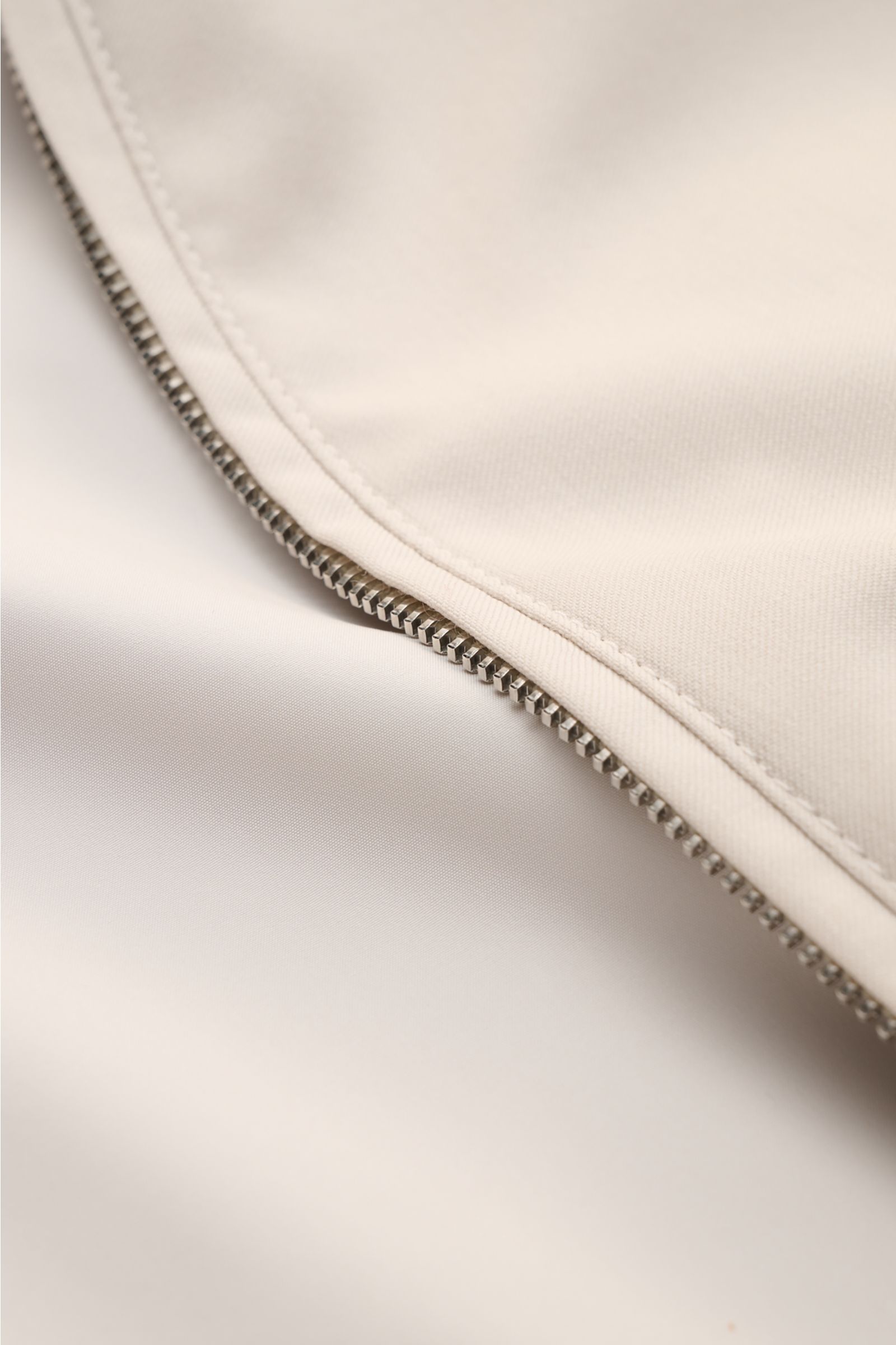 Nahaufnahme des zwei-Wege-Metallreißverschlusses am Mandelli Blouson beige aus glatter, reiner Wolle mit elastischem Saum.