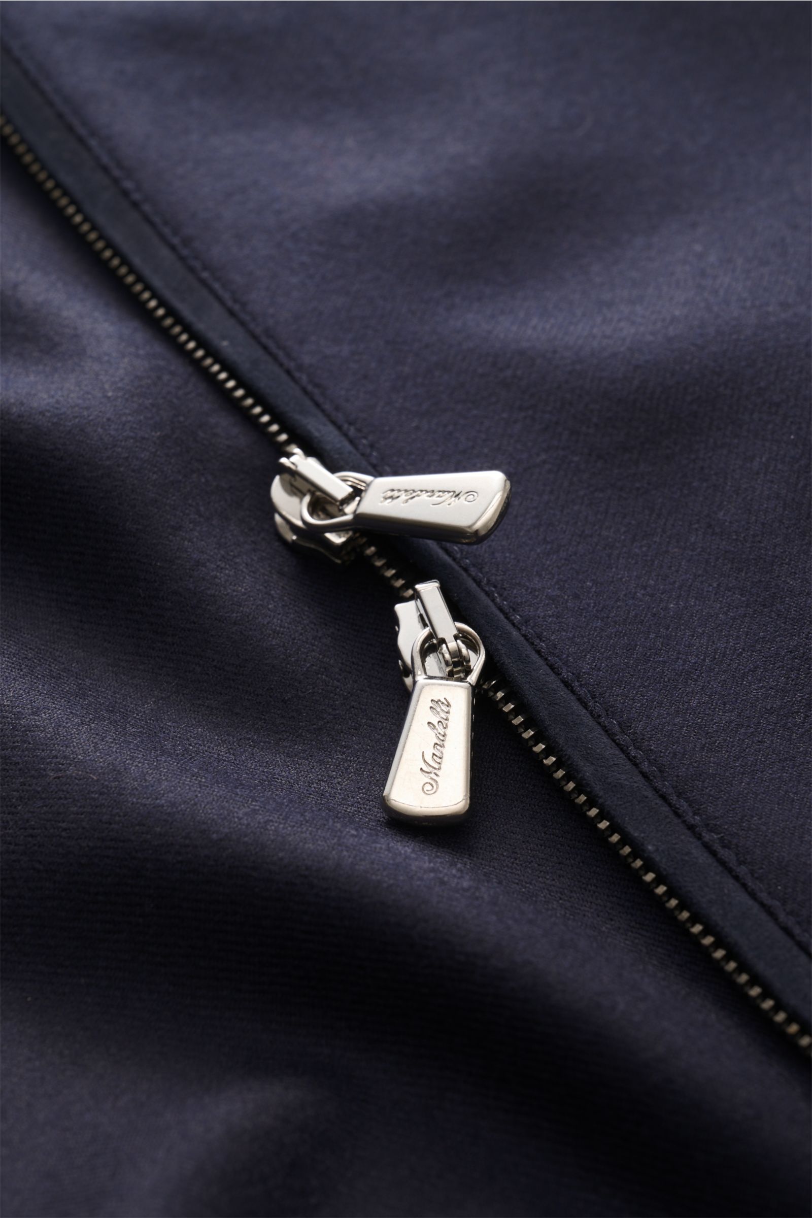 Close-up top-down view of the two-way silver zipper with Mandelli logo on the navy fabric of the Mandelli Cashmere blouson navy, showcasing pure cashmere material, soft feel, slim fit, standing collar, elastic hem and sleeve cuffs, half lined, and two ins