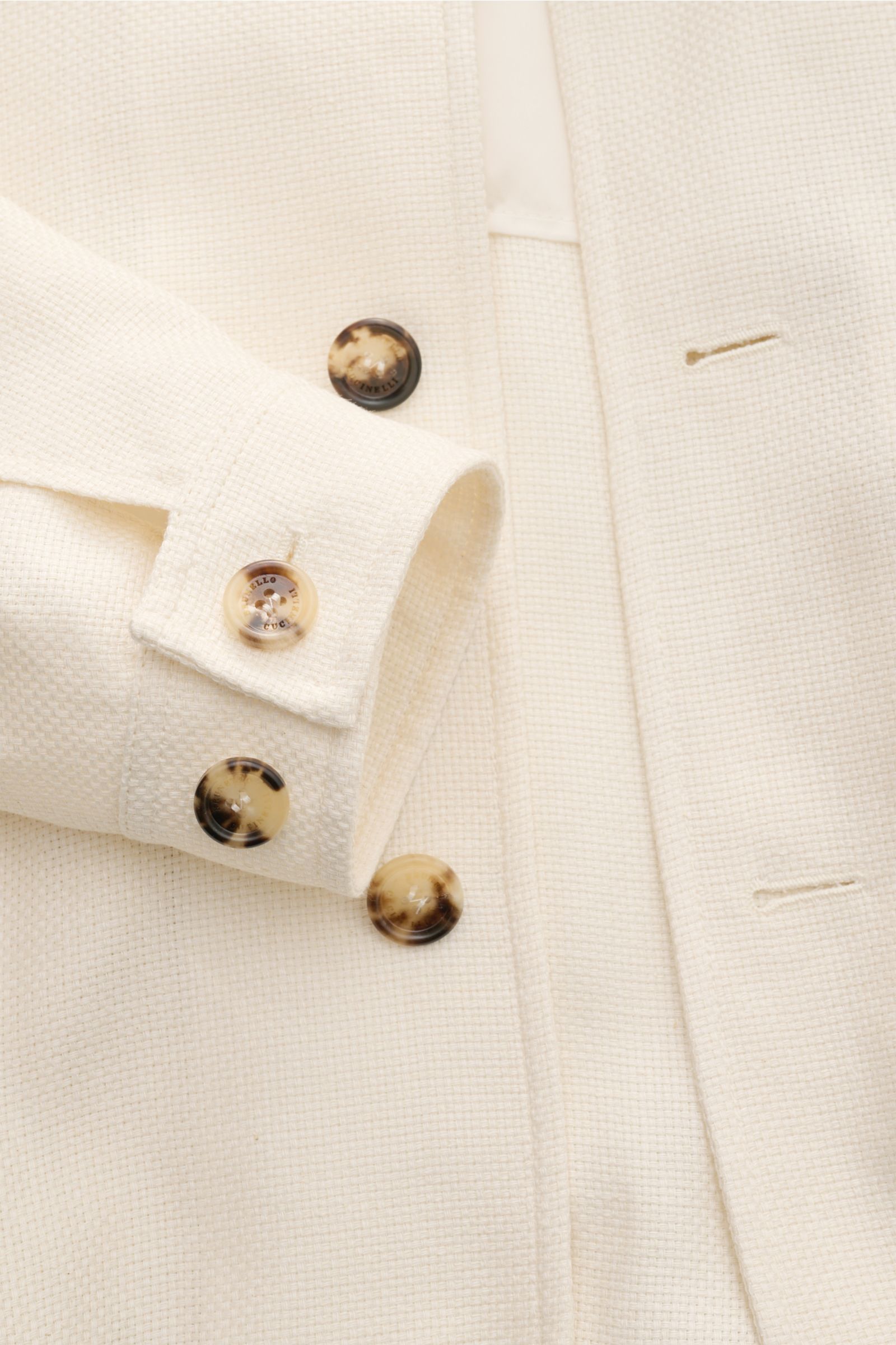 Close-up front view of the Brunello Cucinelli Blouson creme showing its seven-button placket, elastic hem, and soft silk, linen, and wool blend with three-dimensional weave.