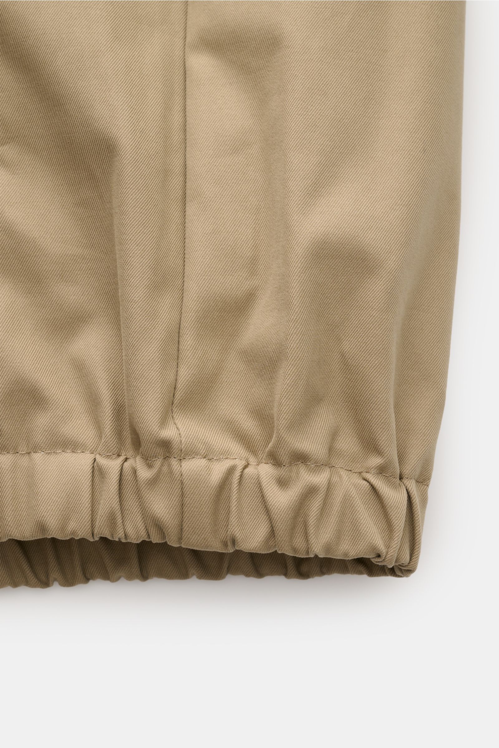 Close-up front view of the elastic hem of the Ami Paris Blouson taupe, made of pure cotton with a soft touch, Slim Fit, two-way zipper, turn-down collar, logo stitching on the chest, slanted welt pockets, elastic hem and cuffs, and one inside pocket, a st