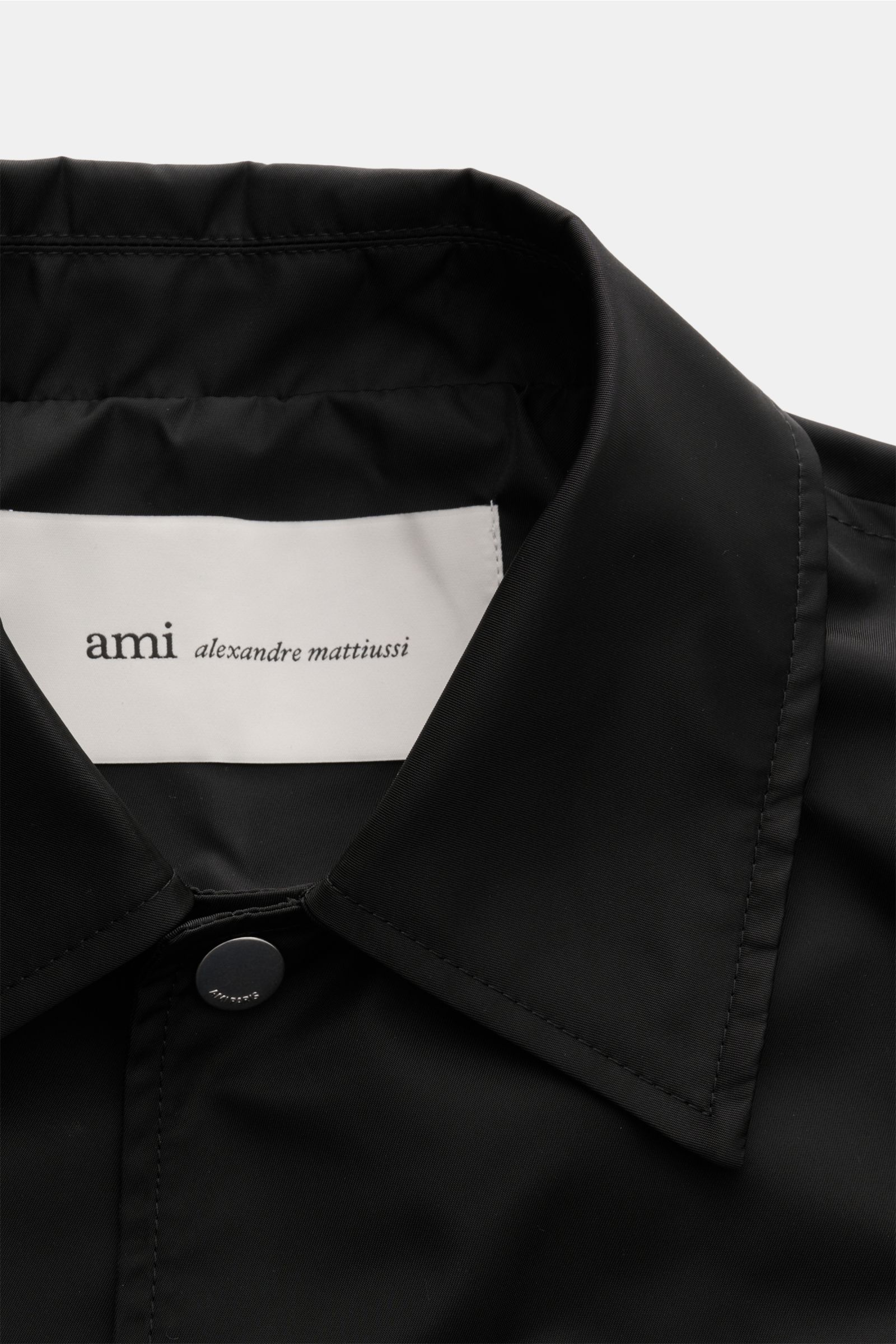 Close-up front view of the Ami Paris Jacke schwarz showing a smooth microfiber fabric, regular fit, snap button placket, and classic collar. Stilvoll durch die Übergangszeit: Die AMI PARIS Jacke besticht mit legerem Schnitt und vielseitigen Kombinationsmö