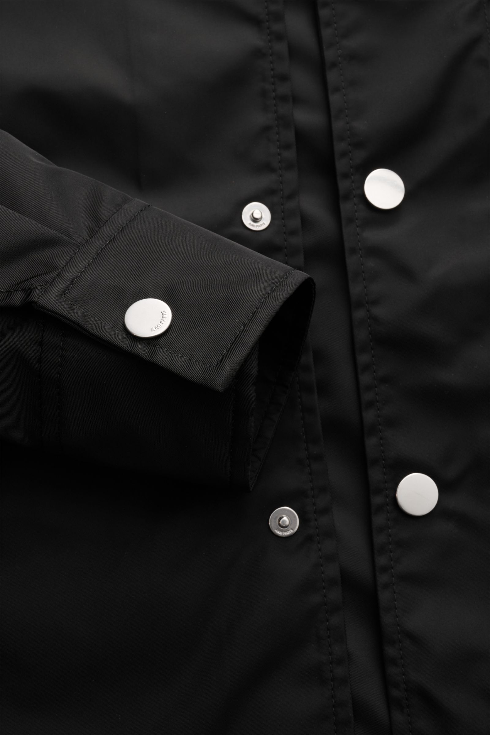 Close-up front view of the Ami Paris Jacke schwarz showcasing its black microfiber fabric, smooth texture, snap button placket, and cuff details.