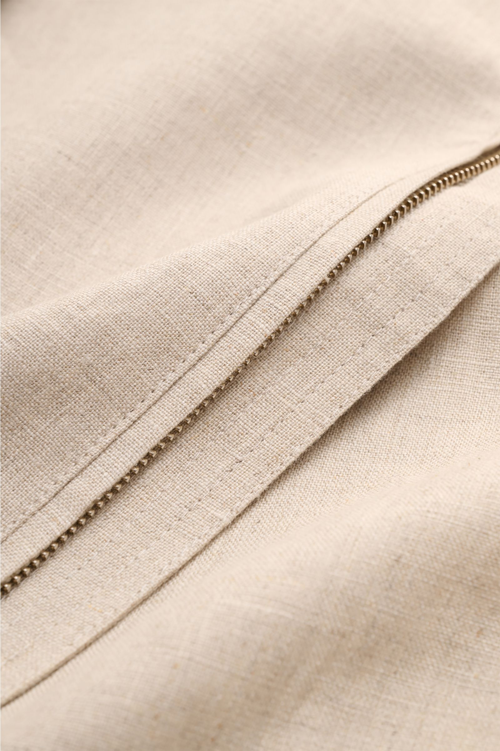 Nahaufnahme des robusten Reißverschlusses und der fein gewebten Leinenstruktur des Ché Blouson 'Benito' beige meliert.