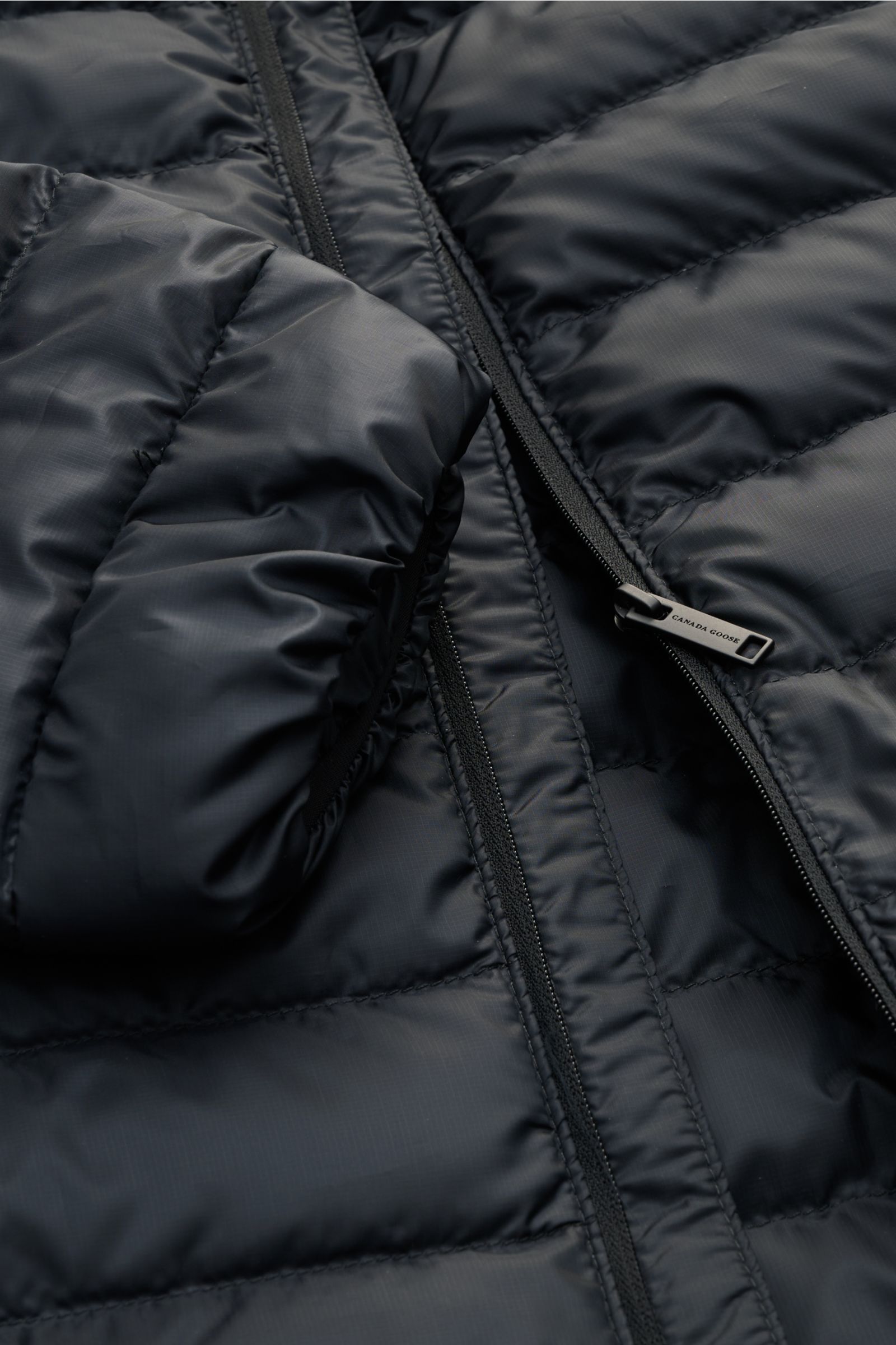 Close-up front view of Canada Goose Down jacket 'Stratus Tonal' navy, showing ripstop fabric, zipper, and padded collar details.

The super lightweight 'Stratus Tonal' down jacket by CANADA GOOSE with high-quality ripstop outer material is self-stowing