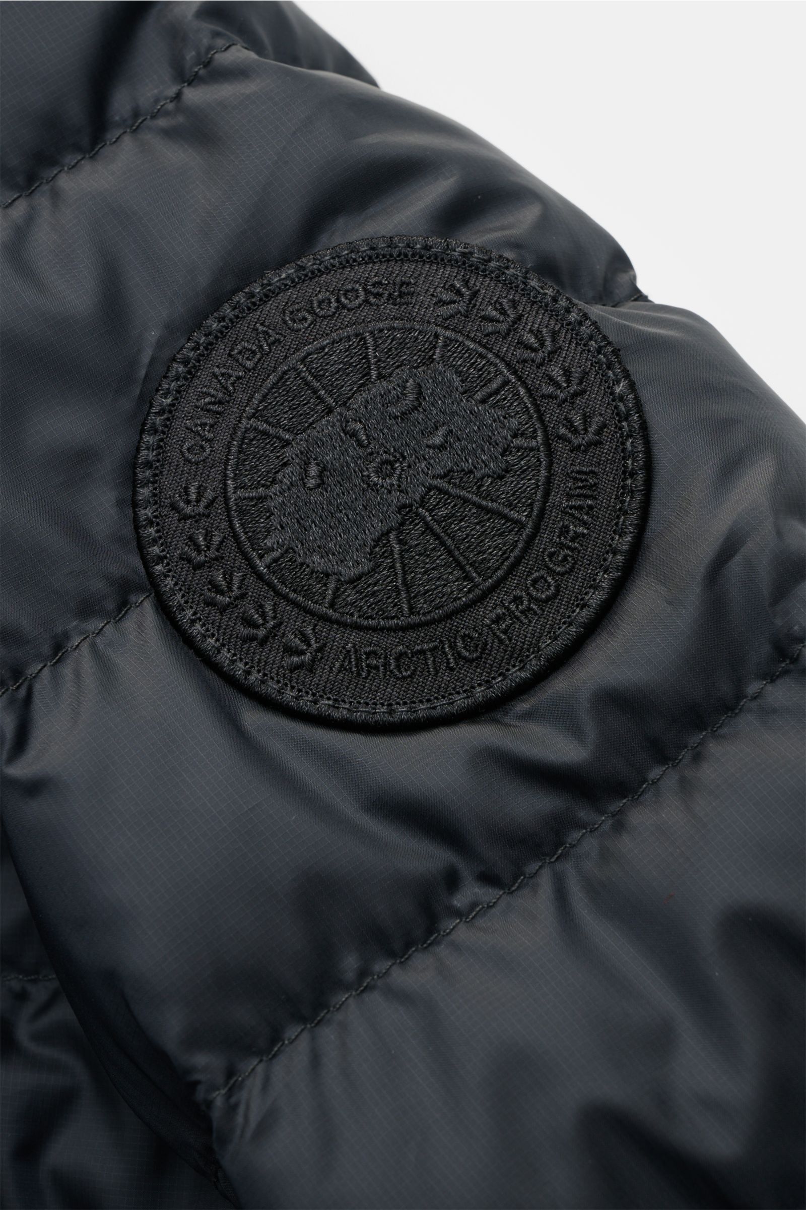Close-up view of the Canada Goose Down jacket 'Stratus Tonal' navy showing the tonal woven logo patch on the sleeve with ripstop microfiber fabric. The super lightweight 'Stratus Tonal' down jacket by CANADA GOOSE features a smooth, wind and water repelle