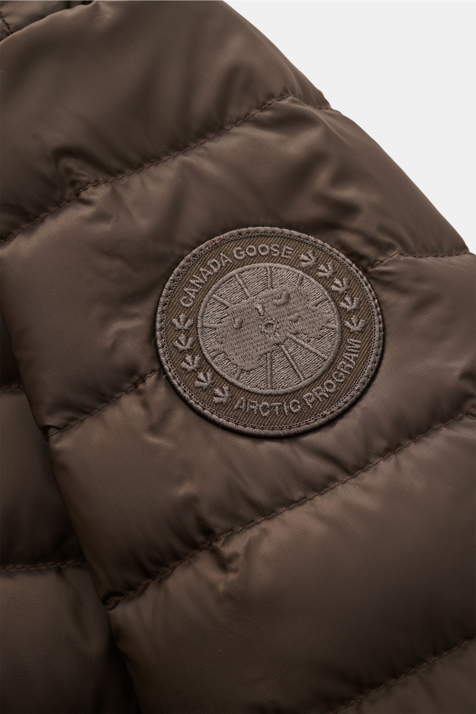 Close-up view of the Canada Goose Down jacket 'Stratus Tonal' dark brown showing the tonal embroidered logo patch on the sleeve.

Description: The super lightweight 'Stratus Tonal' down jacket by CANADA GOOSE with high-quality ripstop outer material is