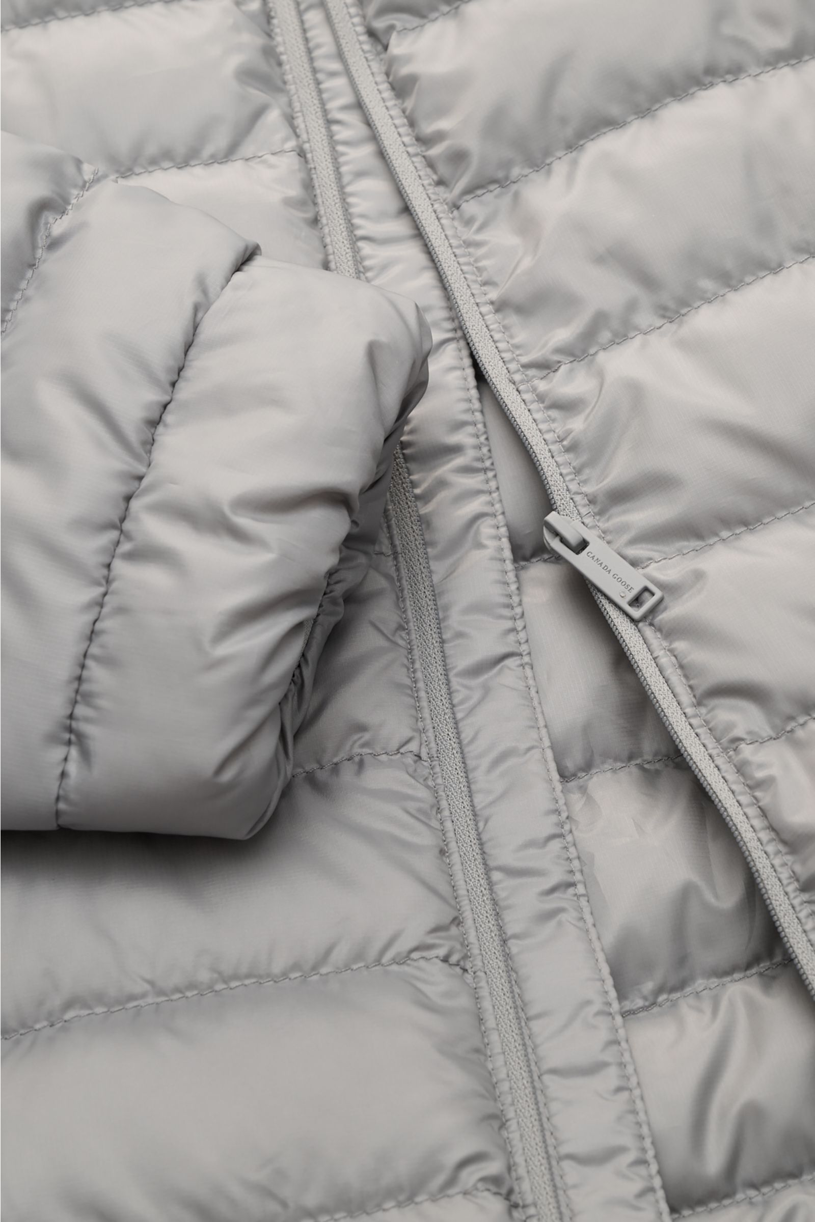 Close-up front view of Canada Goose Down jacket 'Stratus Tonal' light grey, showing ripstop fabric, slim fit, padded collar, and zip detail.

The super lightweight 'Stratus Tonal' down jacket by CANADA GOOSE with high-quality ripstop outer material is 