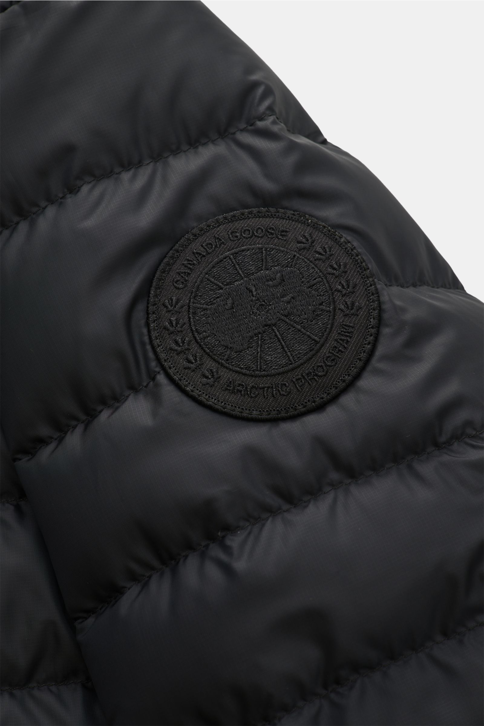Nahaufnahme der schwarzen Canada Goose Daunenjacke 'Stratus Hoody' mit Ripstop-Obermaterial, tonalem Weblabel am Oberarm, fotografiert aus seitlicher Perspektive.