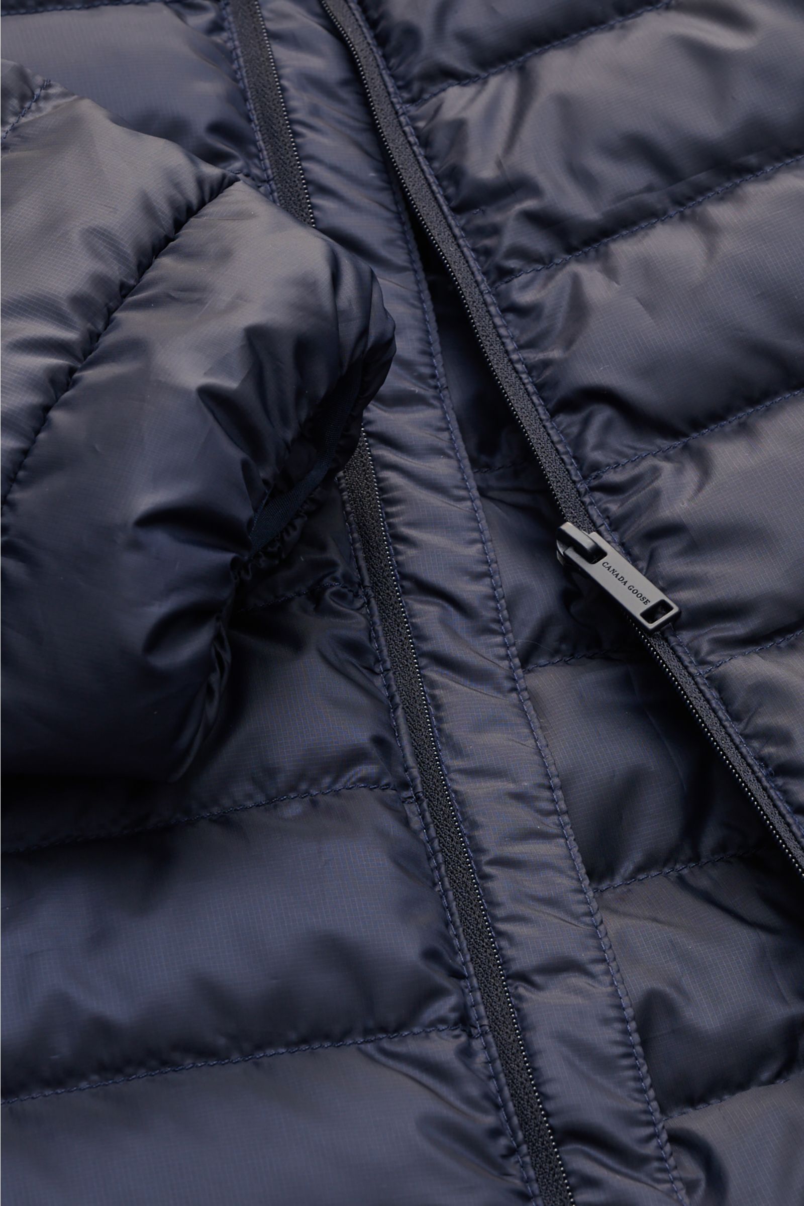 Close-up front view of the Canada Goose Down jacket 'Stratus Hoody' navy, showing detailed stitching, ripstop fabric, and zipper pull. The lightweight down jacket 'Stratus Hoody' by CANADA GOOSE with high-quality ripstop outer material is self-stowing, ma
