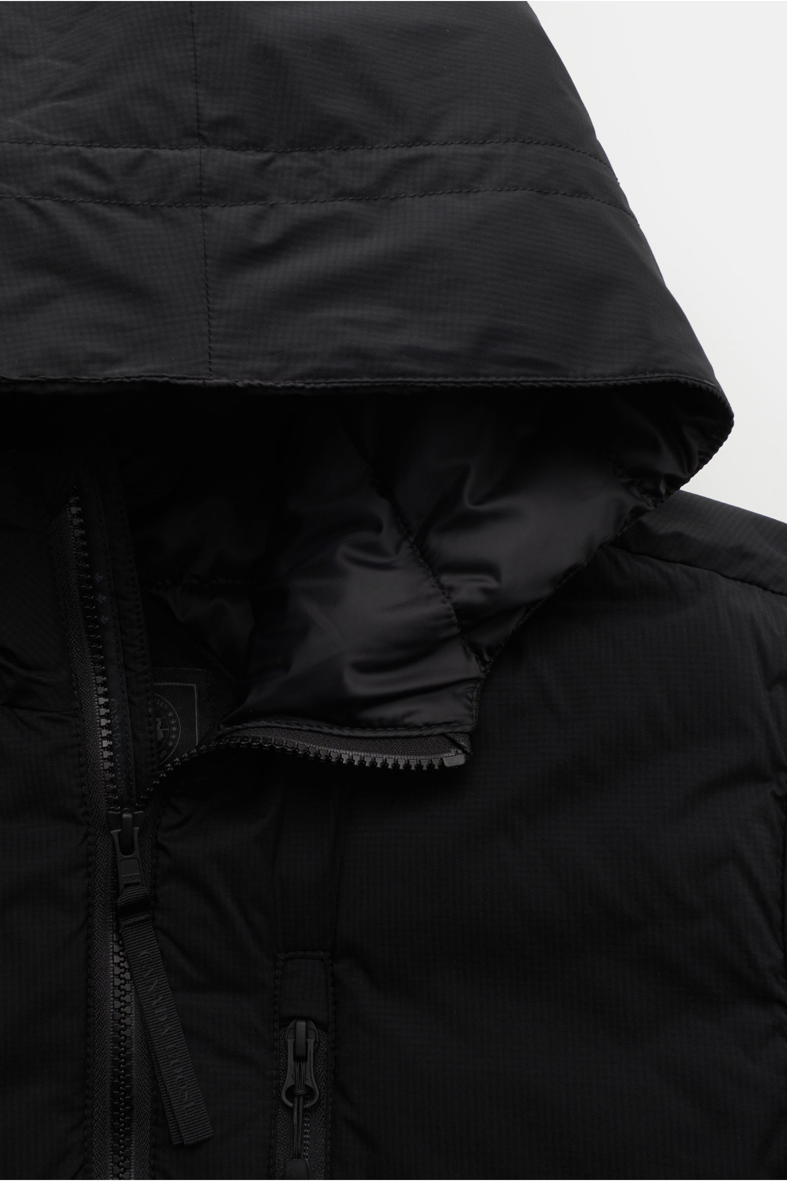 Close-up front view of the black Canada Goose Daunenjacke 'Lodge Hoody' showing hood, two-way zipper, and chest pocket with ripstop fabric, wind- and water-resistant. Maximaler Komfort in leichter Ausführung: Die in sich verstaubare Daunenjacke 'Lodge Hoo