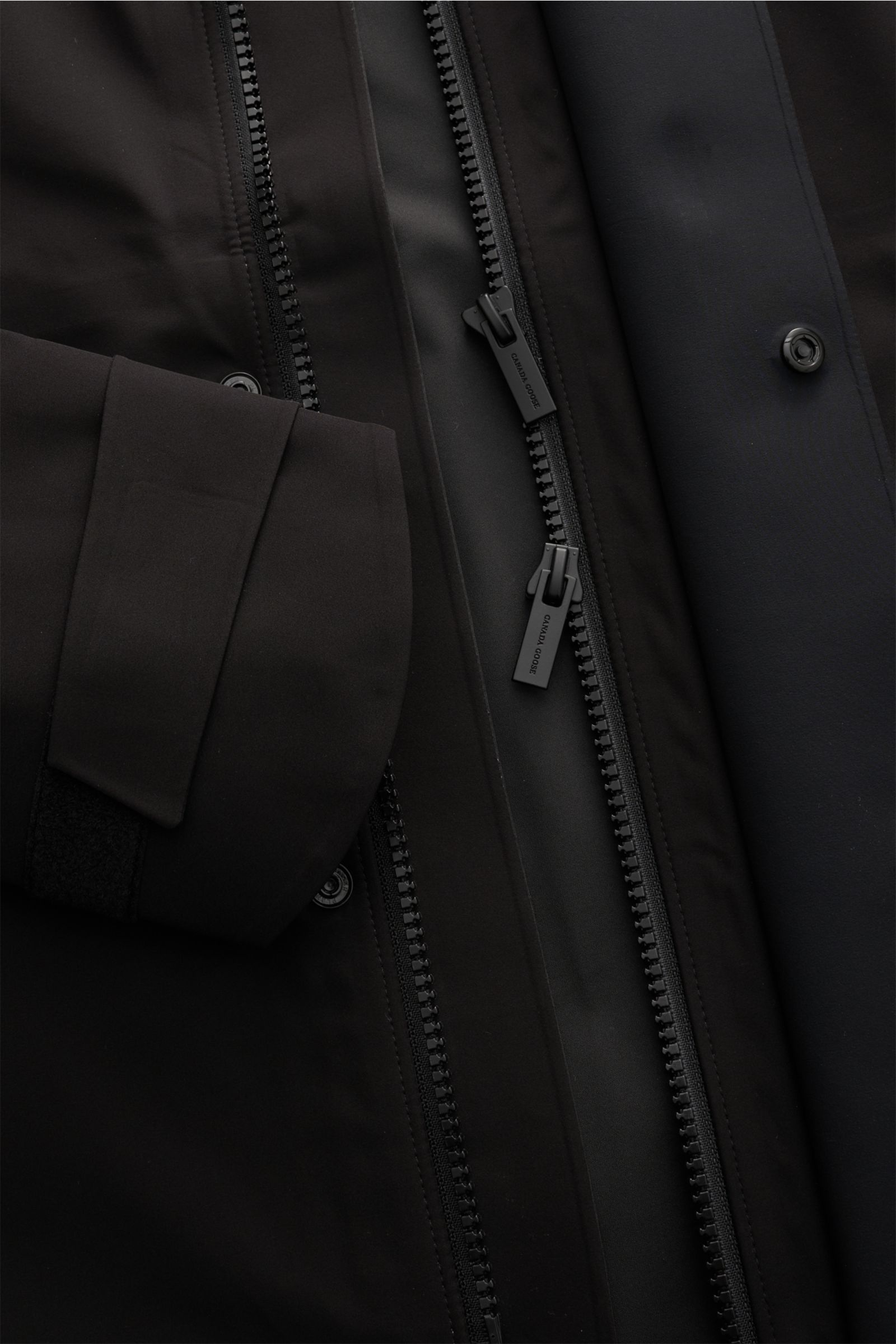 Nahaufnahme der Canada Goose Jacke 'Rupert' schwarz von innen, zeigt Zwei-Wege-Reißverschluss, Ärmelbündchen und Windblende.