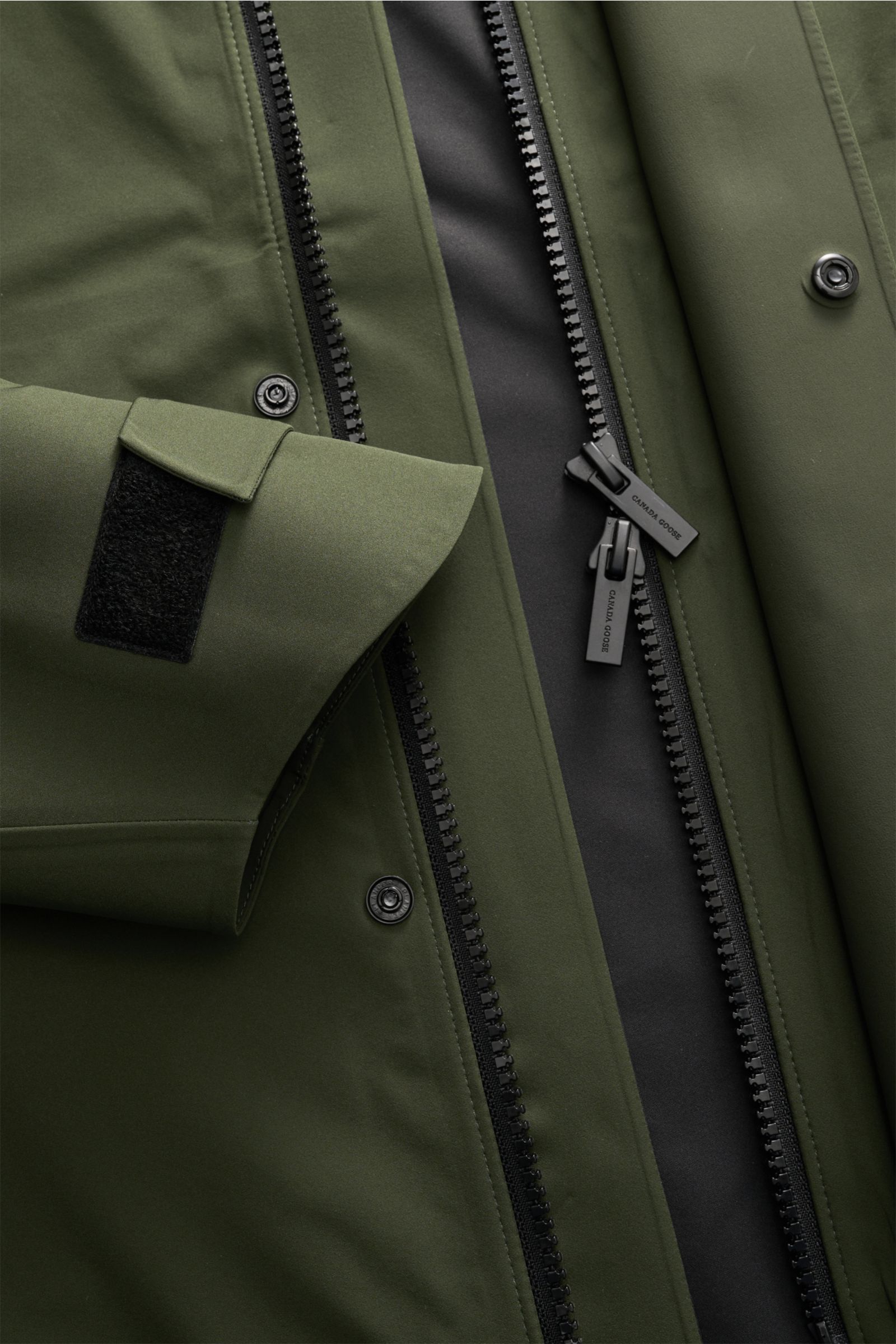 Nahaufnahme der dunkelgrünen Canada Goose Jacke 'Rupert' mit Fokus auf zwei-Wege-Reißverschluss, Klettverschluss am Ärmel und glatter Microfaser-Oberfläche.