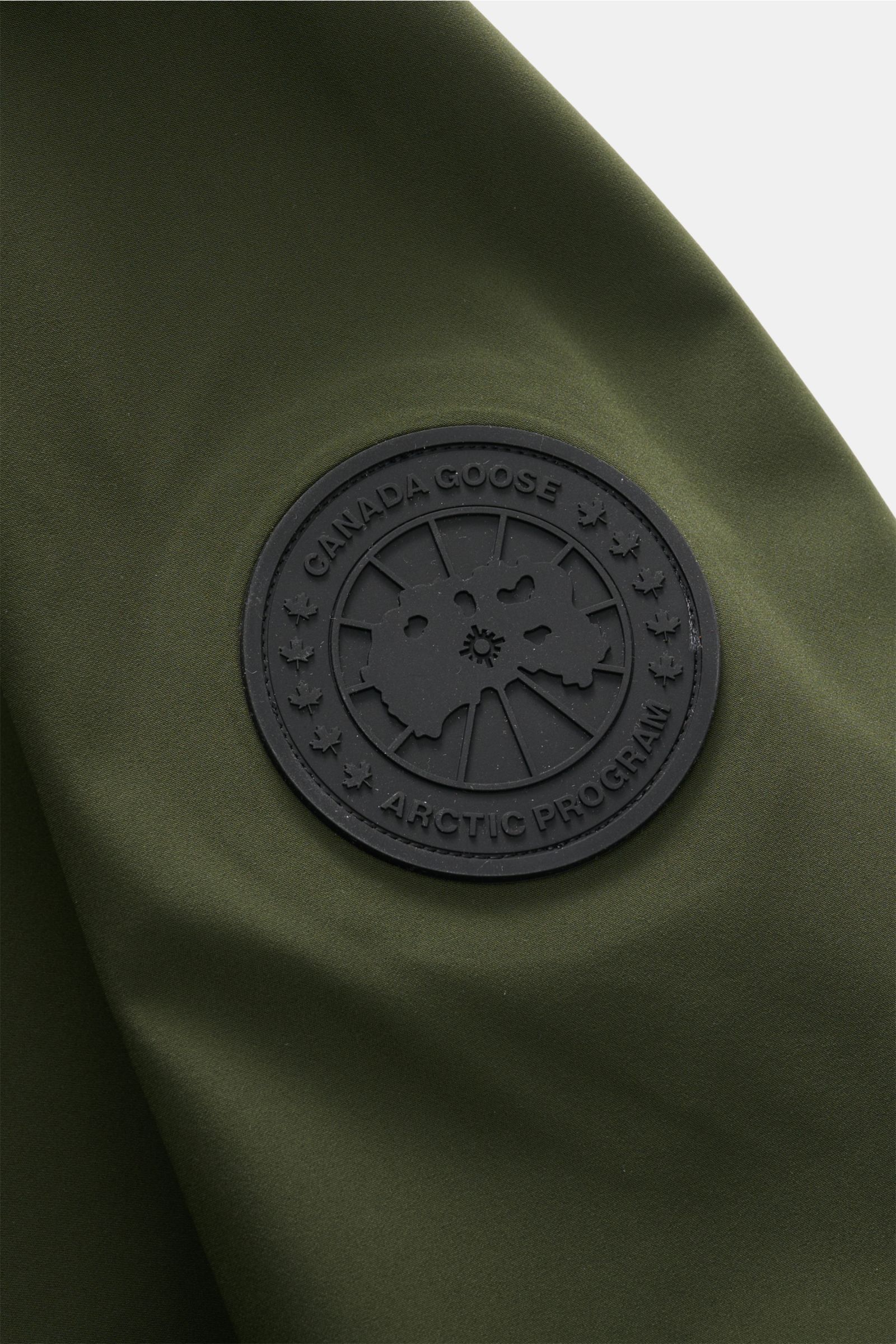 Nahaufnahme des Logos der Canada Goose Jacke 'Rupert' dunkelgrün, funktional mit wasserdichtem Microfaserstoff und atmungsaktivem Komfort.