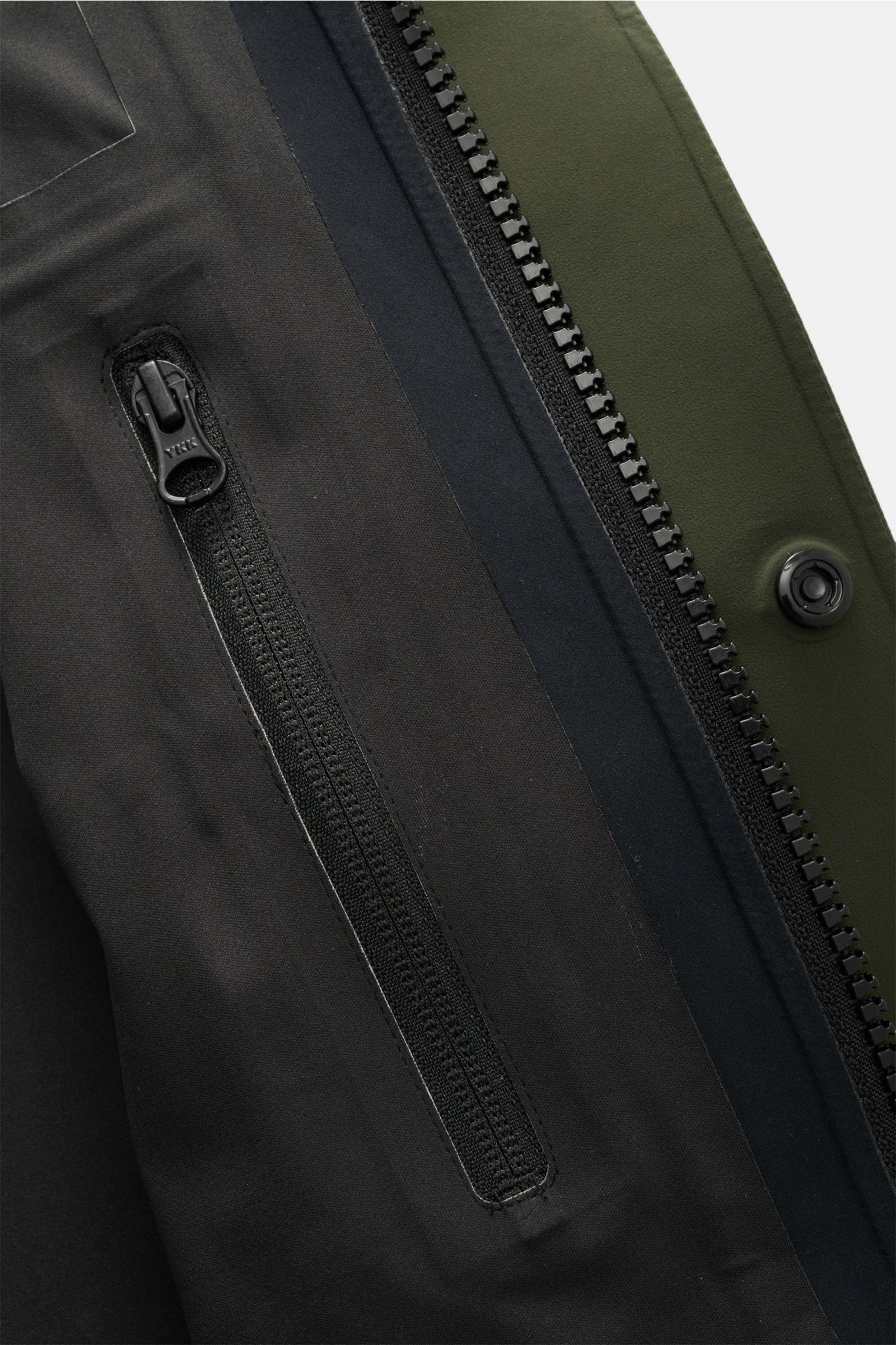 Nahaufnahme aus schräger Perspektive der Reißverschluss- und Druckknopfdetails der Canada Goose Jacke 'Rupert' dunkelgrün, funktional, wasserdicht, Slim Fit.