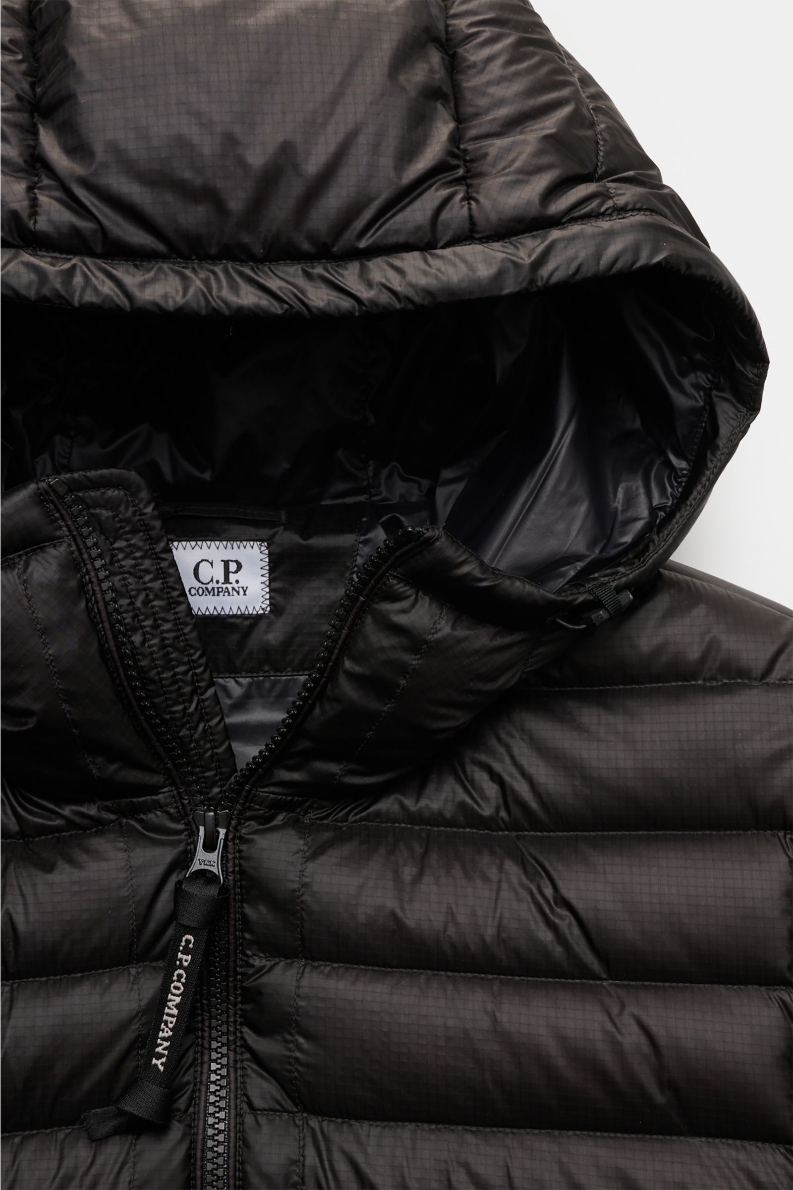 Close-up front view of the C.P. Company Down bomber jacket black, showing high-quality ripstop microfiber with subtle sheen, slim fit, and water-repellent surface, featuring a robust two-way zip with branded pull, high-closing collar, and padded lightweig
