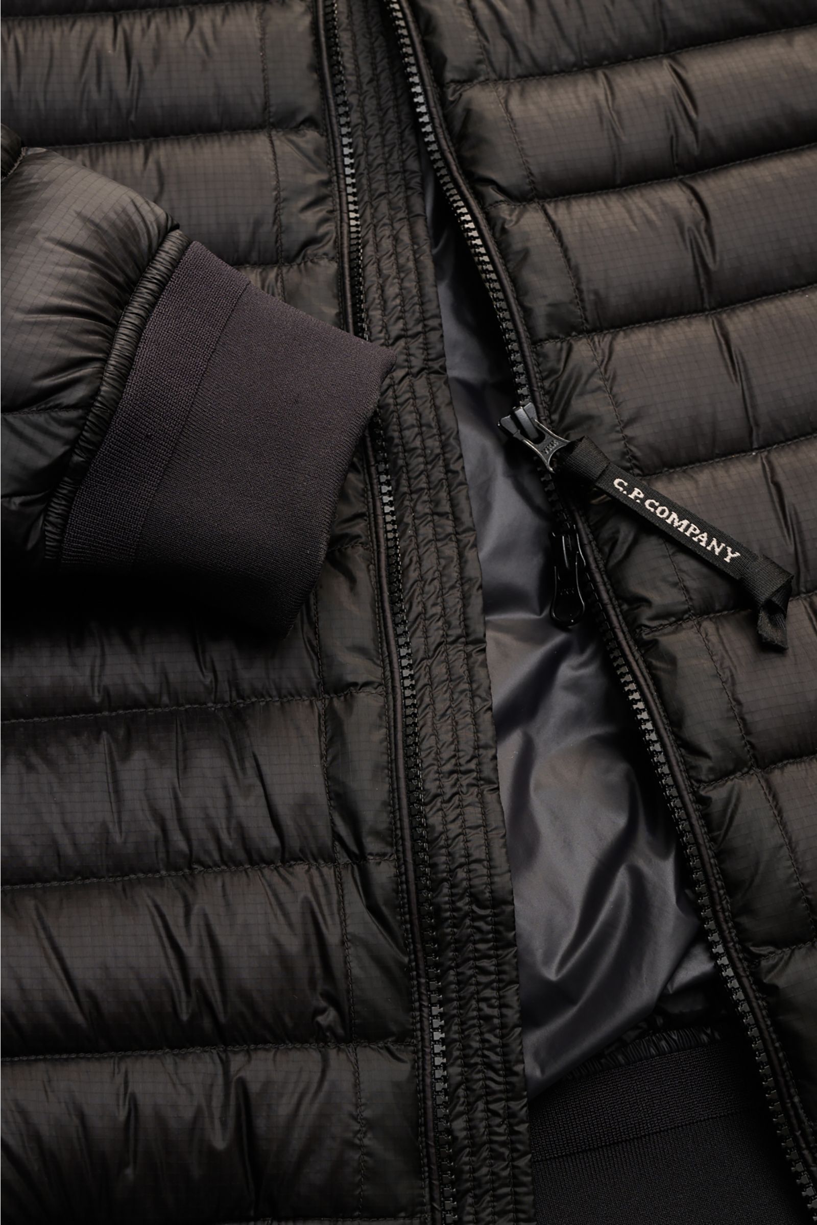 Close-up front view of the C.P. Company Down bomber jacket black showing water repellent ripstop microfiber with subtle sheen, slim fit, elastic cuff, two-way zip with branded pull, and tonal lining. Technical lightness in its most modern form: This blous