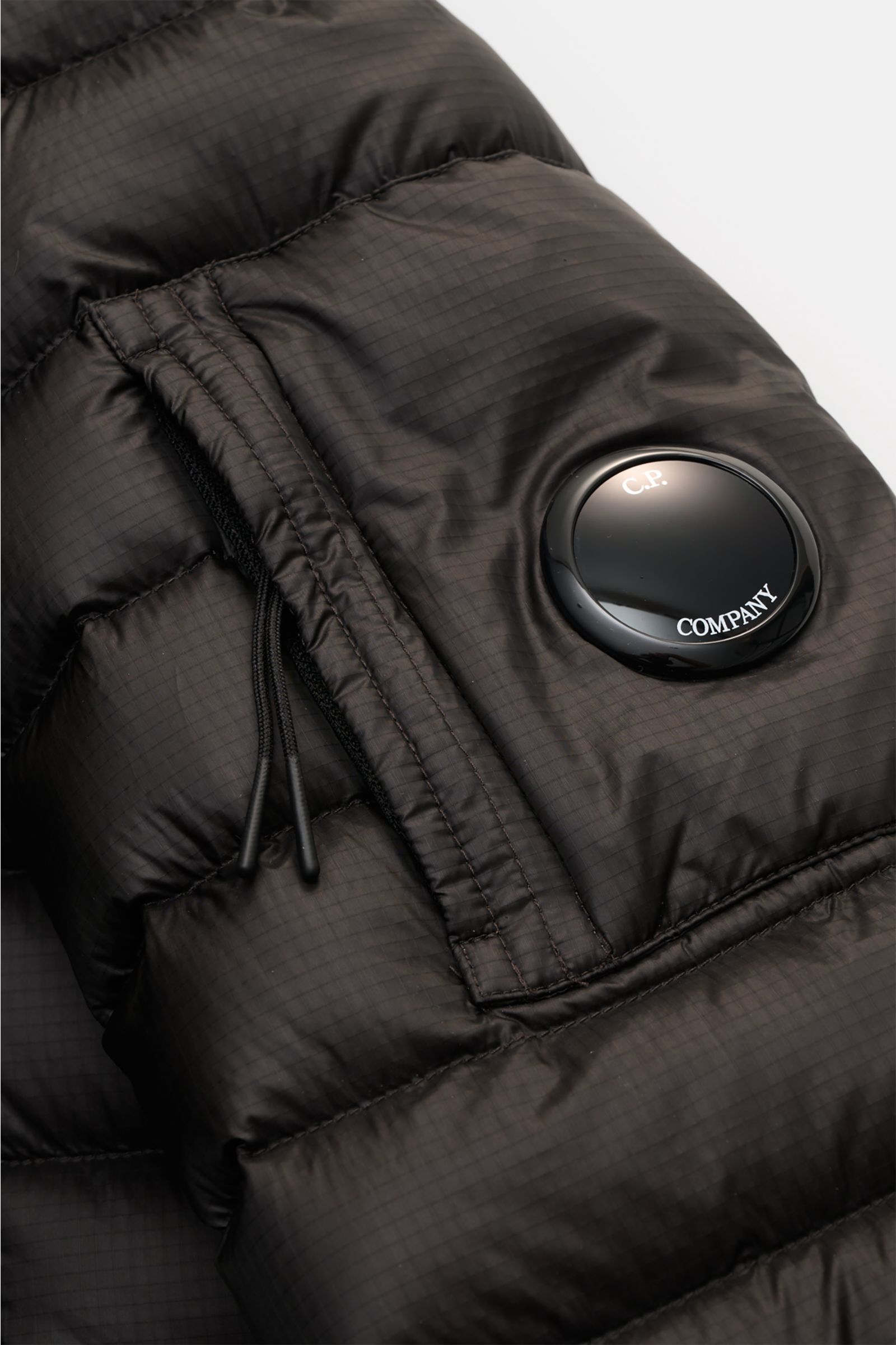 Close-up front sleeve view of the C.P. Company Down bomber jacket black showing water repellent ripstop fabric, slim fit, zipped pocket with signature lens detail, and lightweight down padding. Technical lightness in its most modern form: This blouson by 