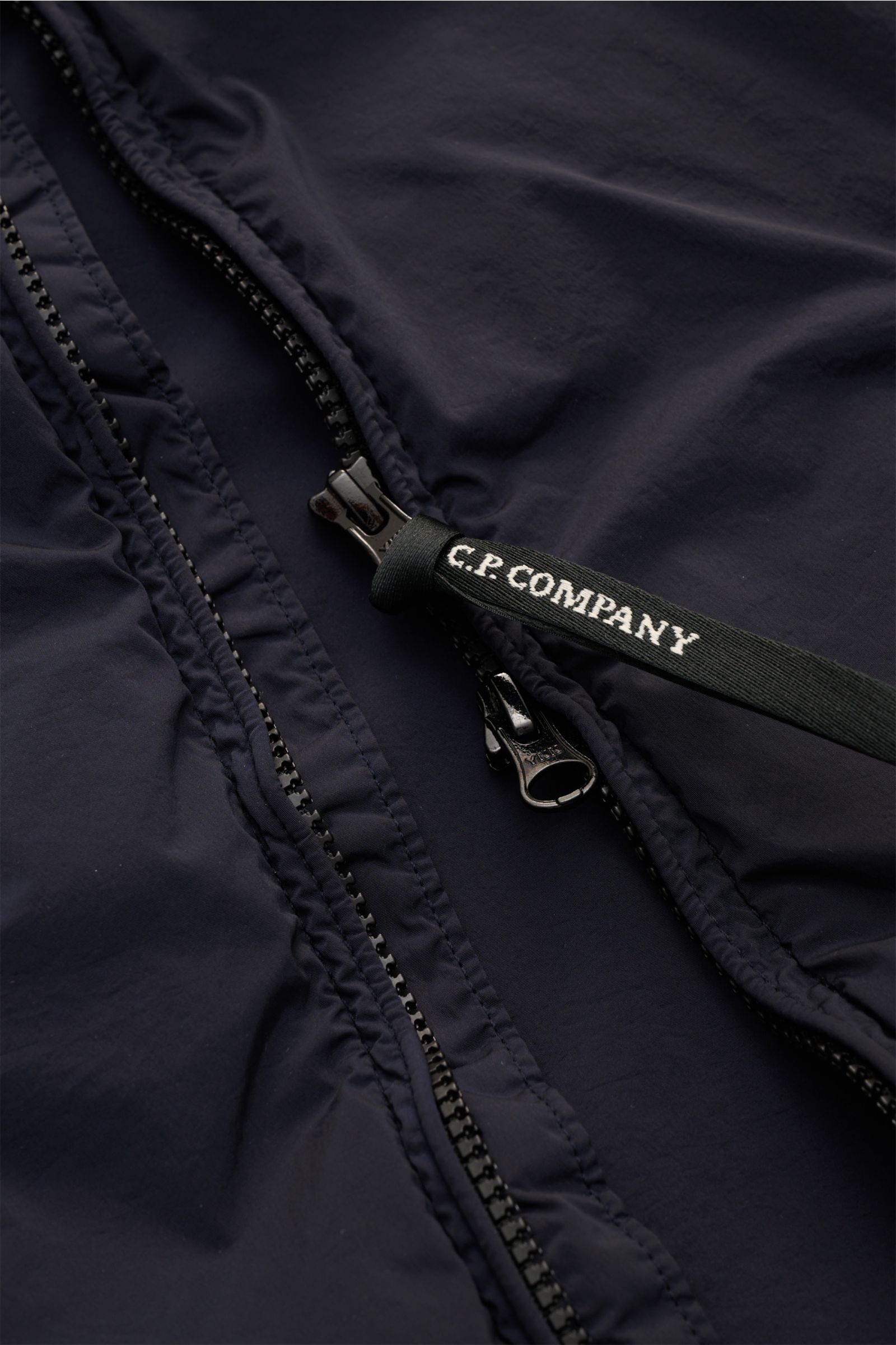 Nahaufnahme des robusten Zwei-Wege-Reißverschlusses vom C.P. Company Blouson 'Nycra R' dark navy aus recycelter Microfaser, wind- und wasserabweisend, slim fit, mit glattem Griff und garment dyed Design.