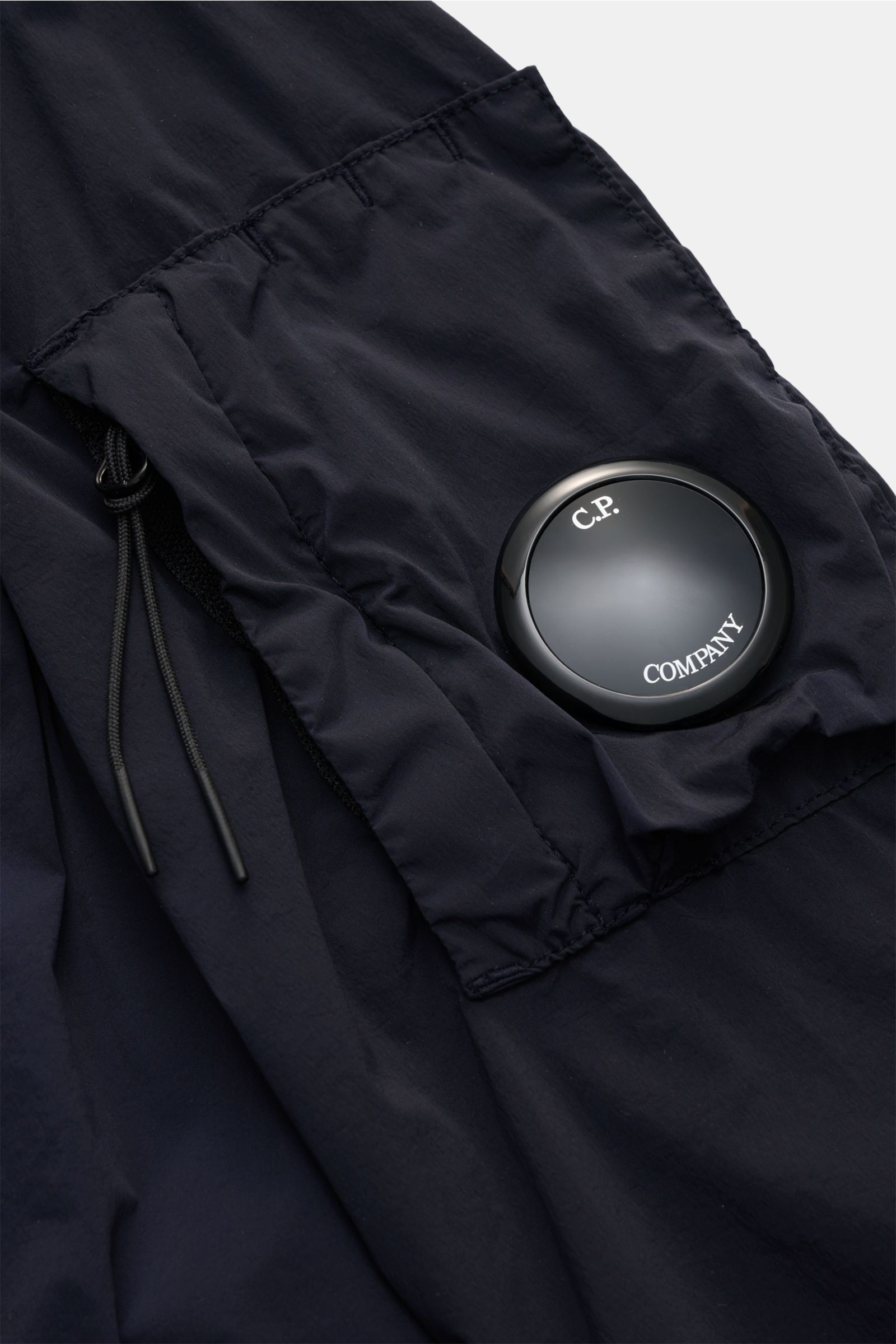 C.P. Company Blouson 'Nycra R' dark navy im Detail, schräg fotografiert, mit Ärmeltasche, Zipper, Linsen-Detail, recycelter Microfaser, wind- und wasserabweisend.