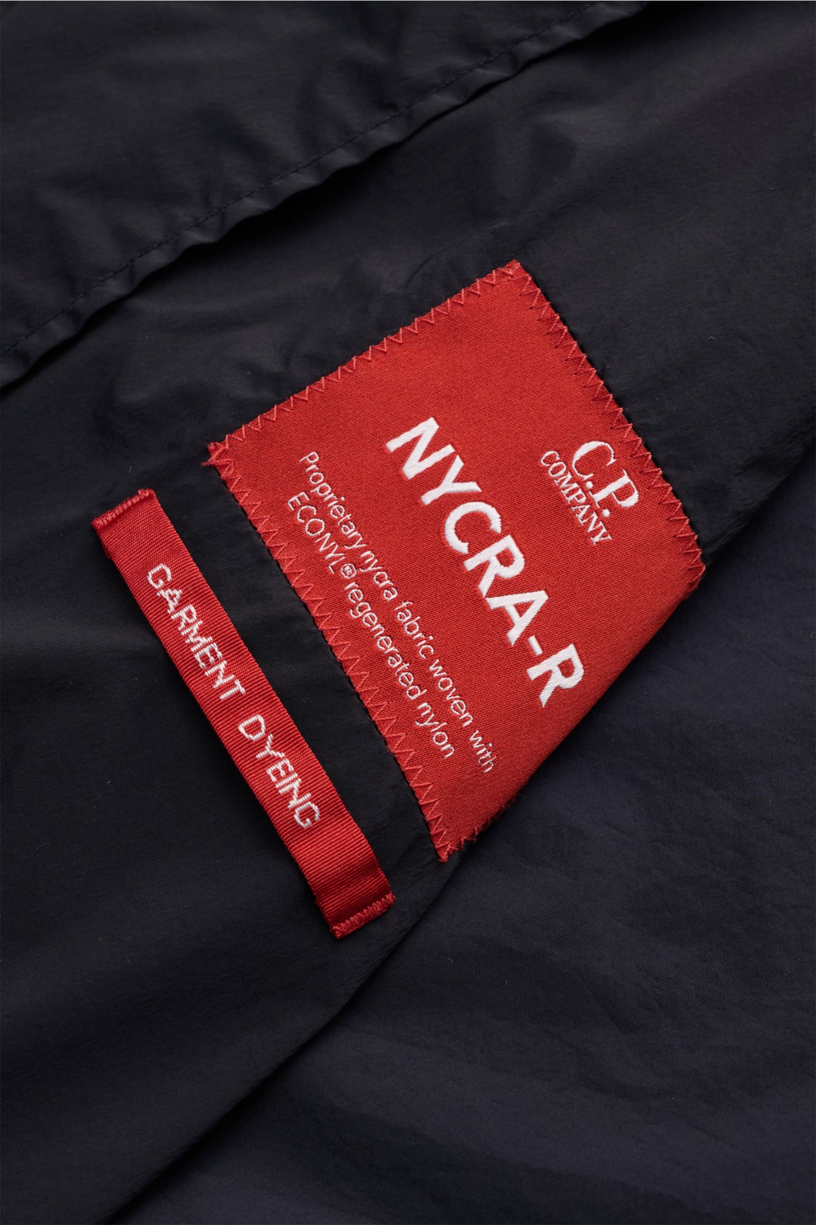 Nahaufnahme des roten Labels auf dem C.P. Company Blouson 'Nycra R' dark navy, recycelte Microfaser, garment dyed, wind- und wasserabweisend.