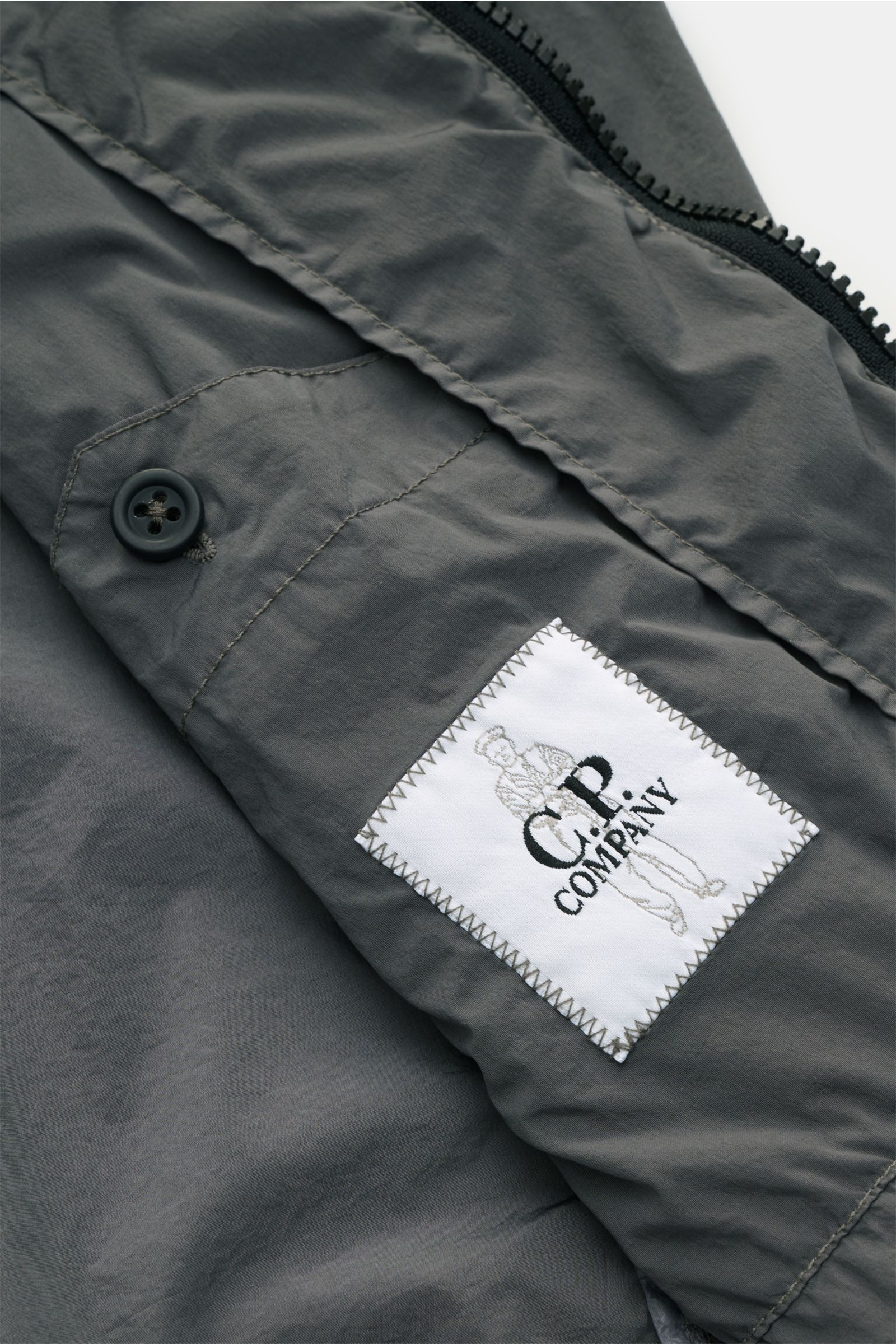 C.P. Company Blouson 'Nycra R' grau, Detailansicht Innenstoff mit Markenlabel, recycelte Microfaser, leicht, wind- und wasserabweisend, Slim Fit.