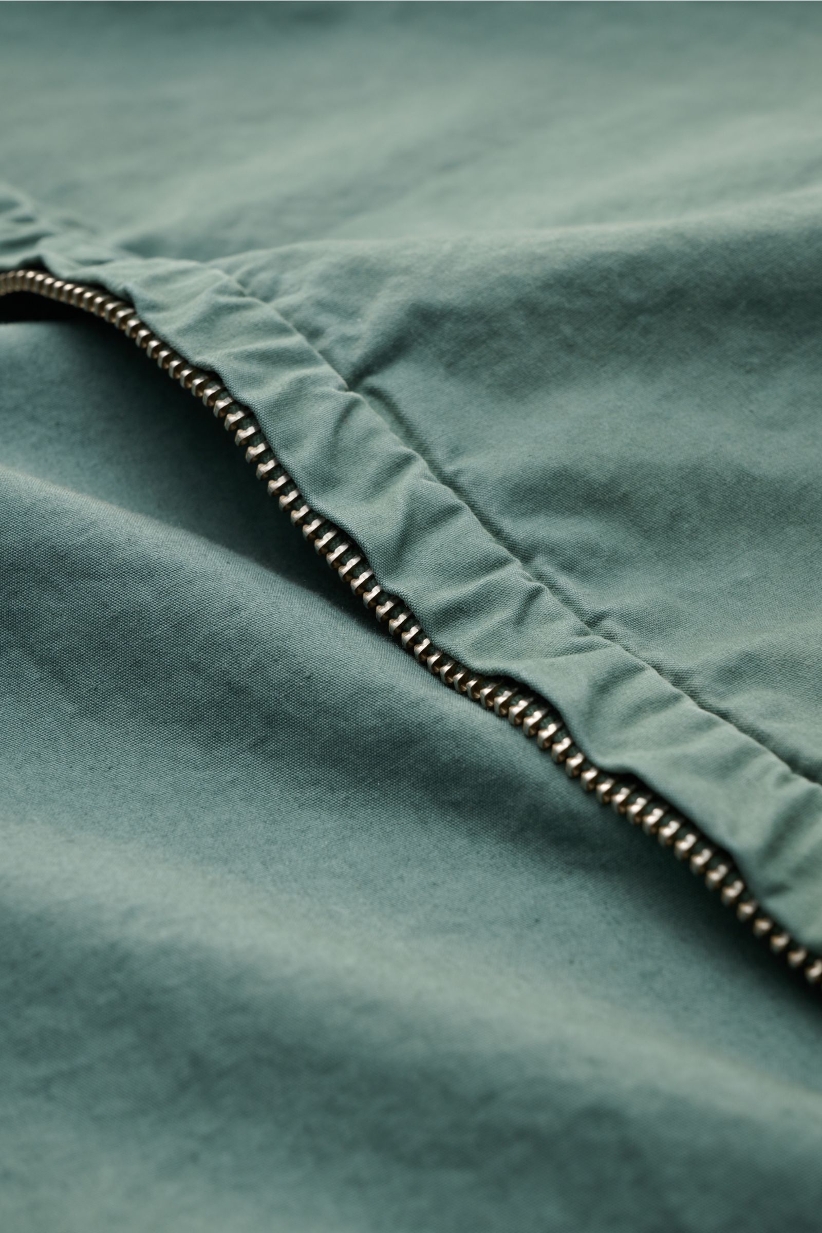 Close-up view of the metal zipper and soft, garment-dyed Micro-Reps fabric of the C.P. Company Jacket sage, highlighting its pure cotton texture and compact structure. Effortlessly urban: This new jacket with hood from C.P. COMPANY is made of Micro-Reps, 