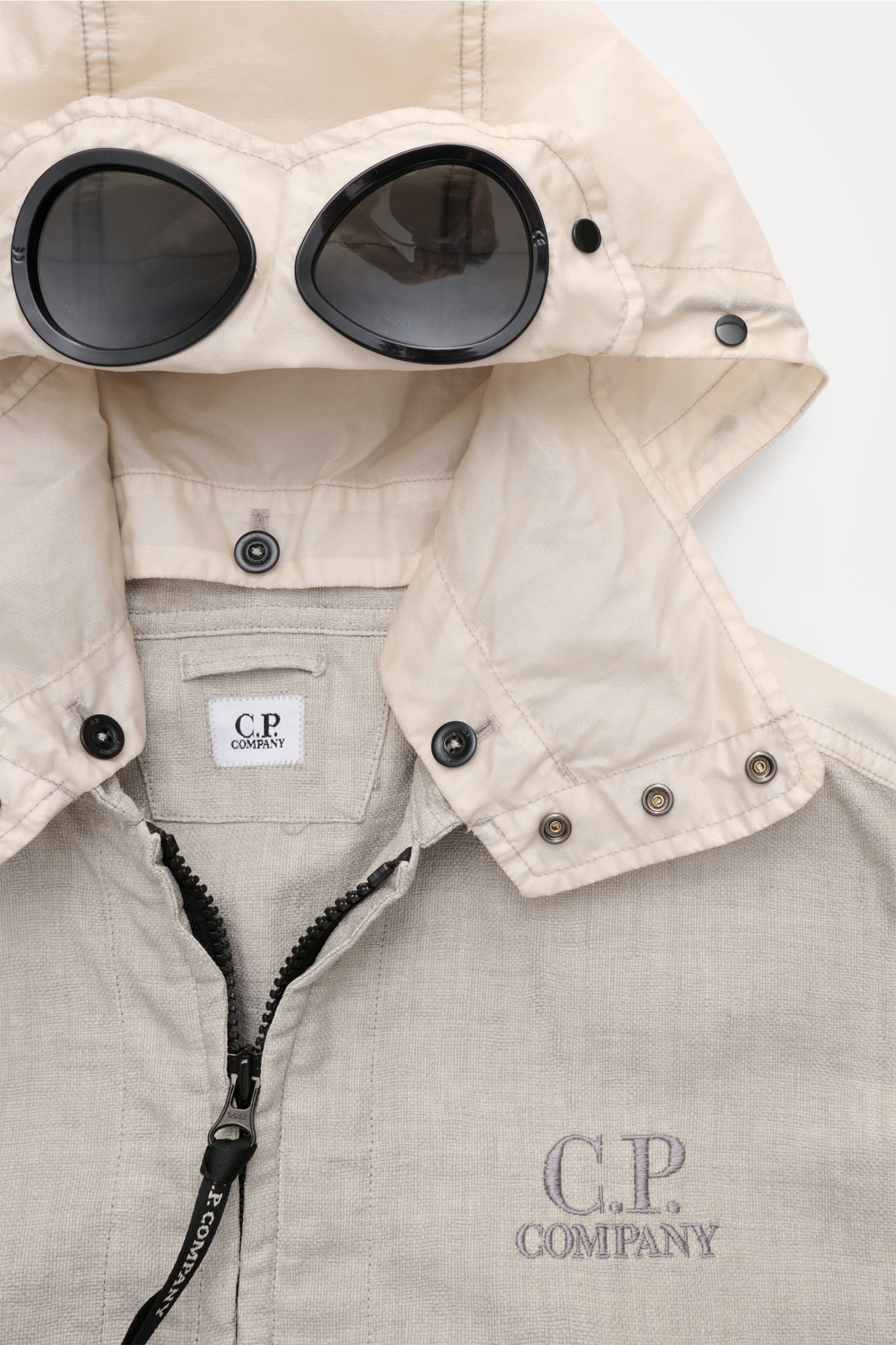 Close-up top-front view of C.P. Company Jacket 'Goggle Jacket' grey, showing detachable hood with integrated black goggle lenses and textured microfibre fabric.

Additional description: 
Signature design from C.P. COMPANY: The 'Goggle Jacket' makes a f