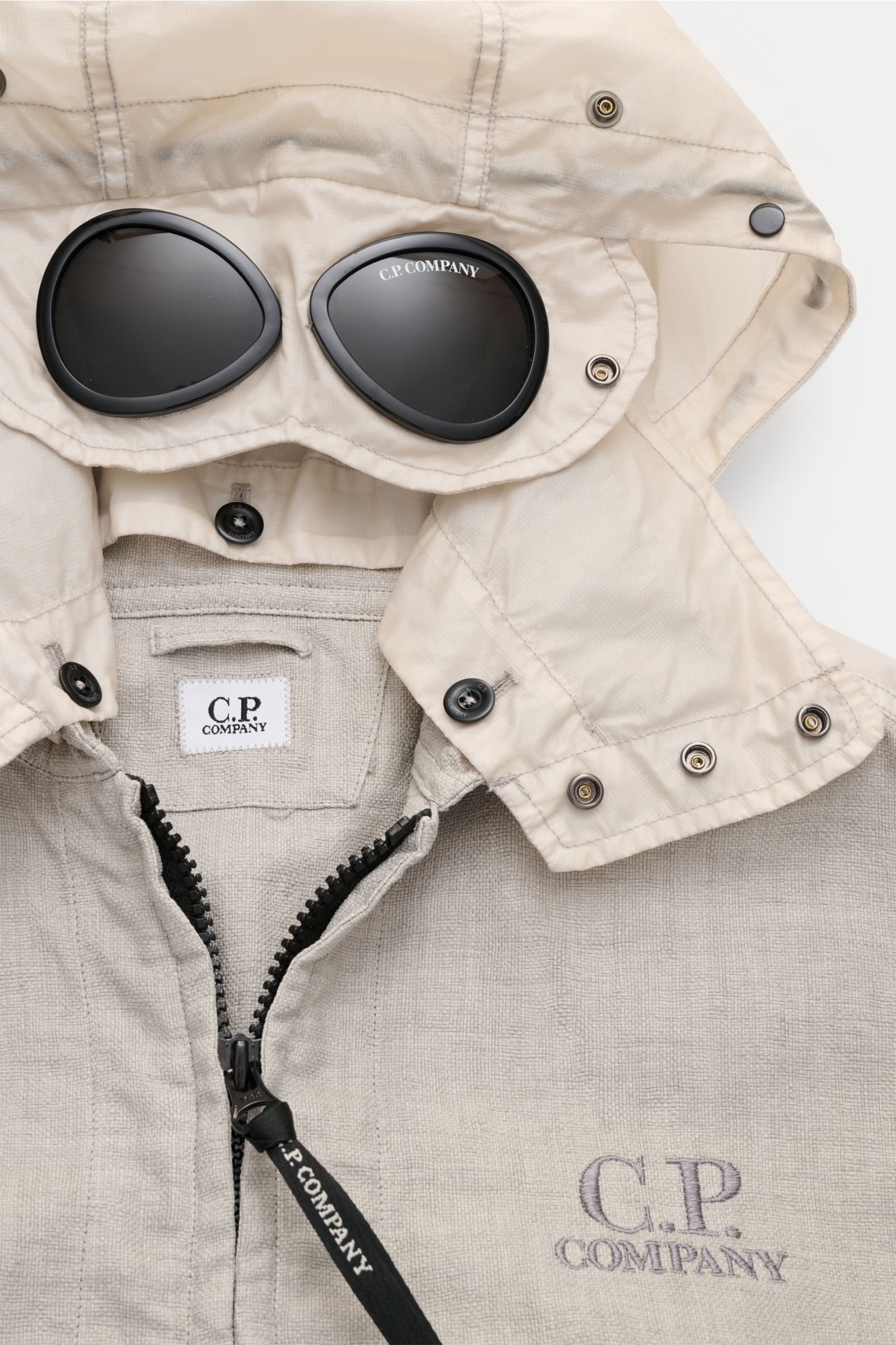 Alt tag (125 characters max):
Close-up front view of C.P. Company Jacket 'Goggle Jacket' grey showing textured fabric, zipper, hood with goggles, and buttons.

Description incorporating provided content:
Signature design from C.P. COMPANY: The 'Goggle 