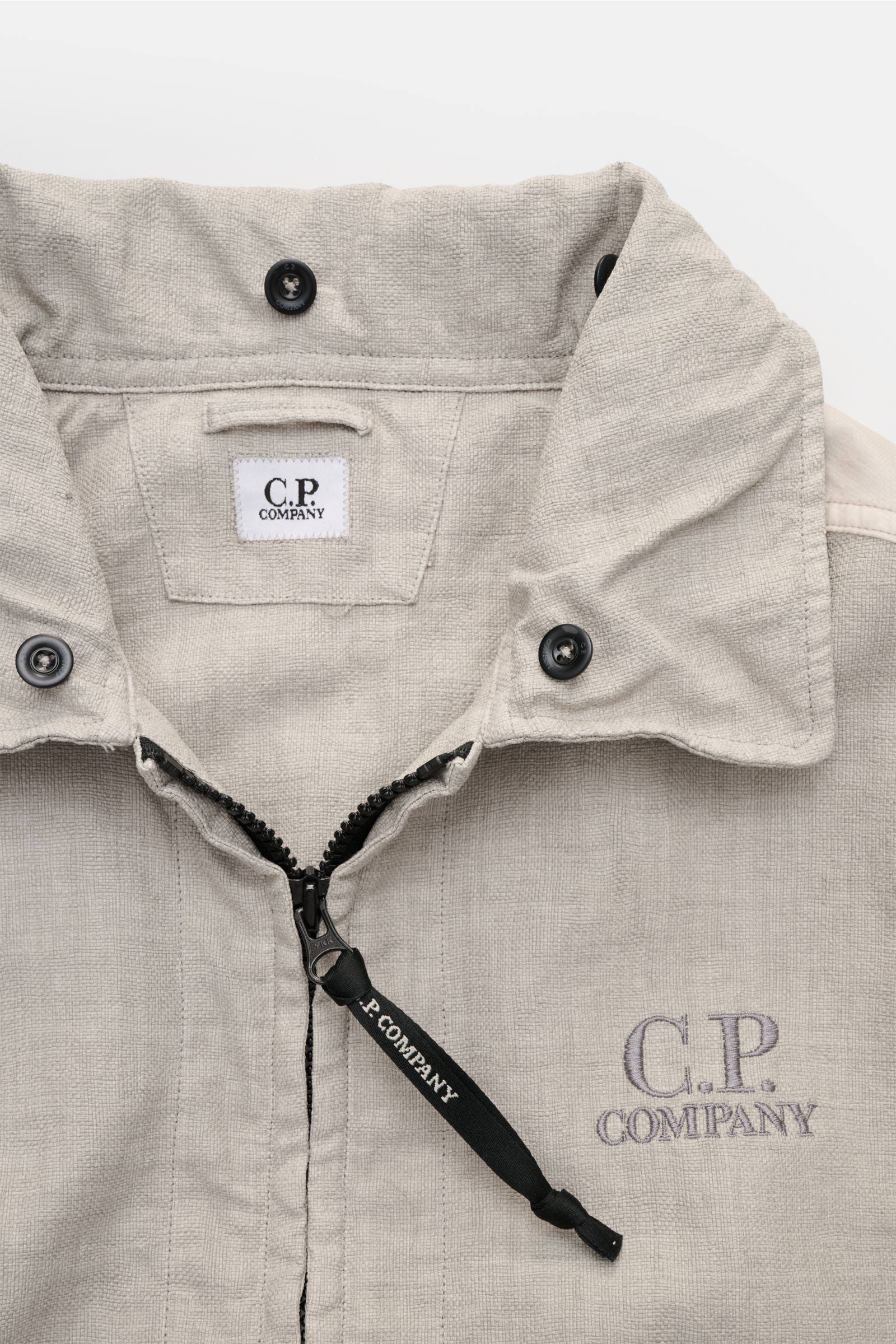 C.P. Company Jacket 'Goggle Jacket' grey close-up from the front top view showing textured microfibre fabric, black button cuffs, zipper with branded pull. Signature design from C.P. COMPANY: The 'Goggle Jacket' makes a futuristic statement with its goggl