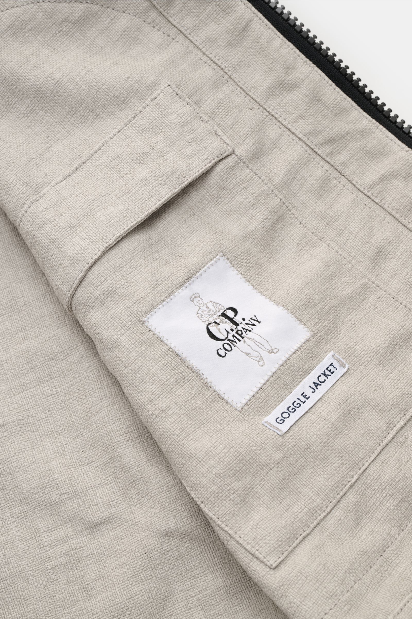 Close-up rear interior view of C.P. Company Jacket 'Goggle Jacket' grey showing textured microfibre fabric, label, and pocket details.

Signature design from C.P. COMPANY: The 'Goggle Jacket' makes a futuristic statement with its goggle lenses integrat