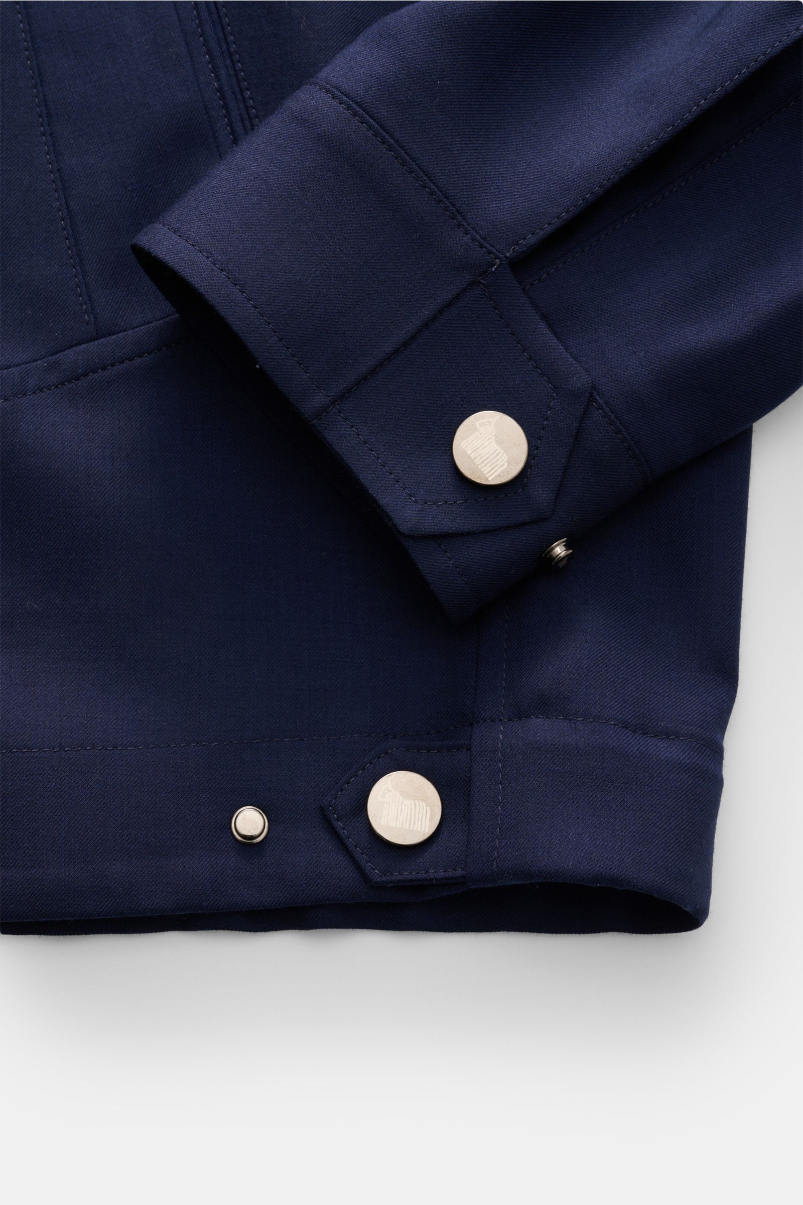 Close-up image of the bottom sleeve and hem of the Colombo Cashmere jacket navy, showing metal buttons and fine stitching from a top-down perspective. An expression of the finest craftsmanship: This cashmere jacket by COLOMBO combines exquisite fabric wit