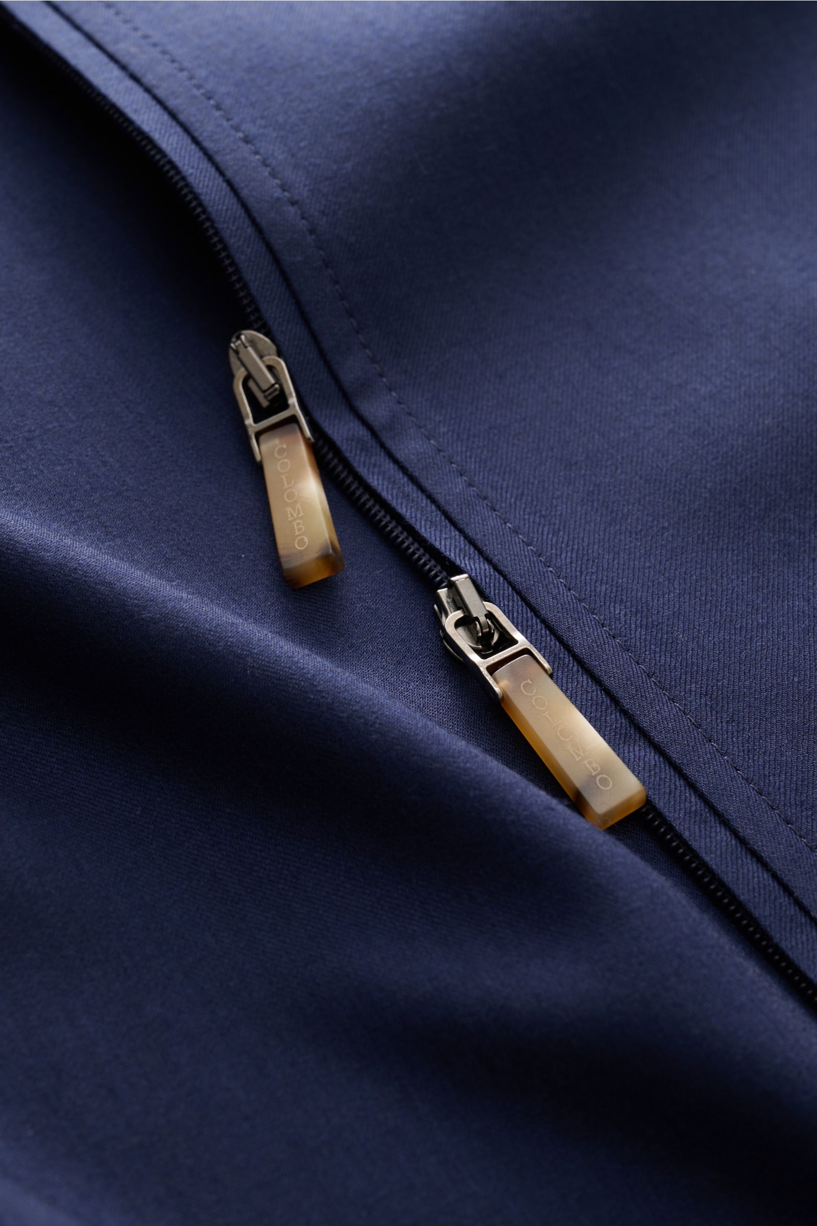 Close-up, angled top-down view of the Colombo Cashmere jacket navy showing its two-way zip with branded sliders on soft, pure cashmere fabric. An expression of the finest craftsmanship: This cashmere jacket by COLOMBO combines exquisite fabric with a flaw